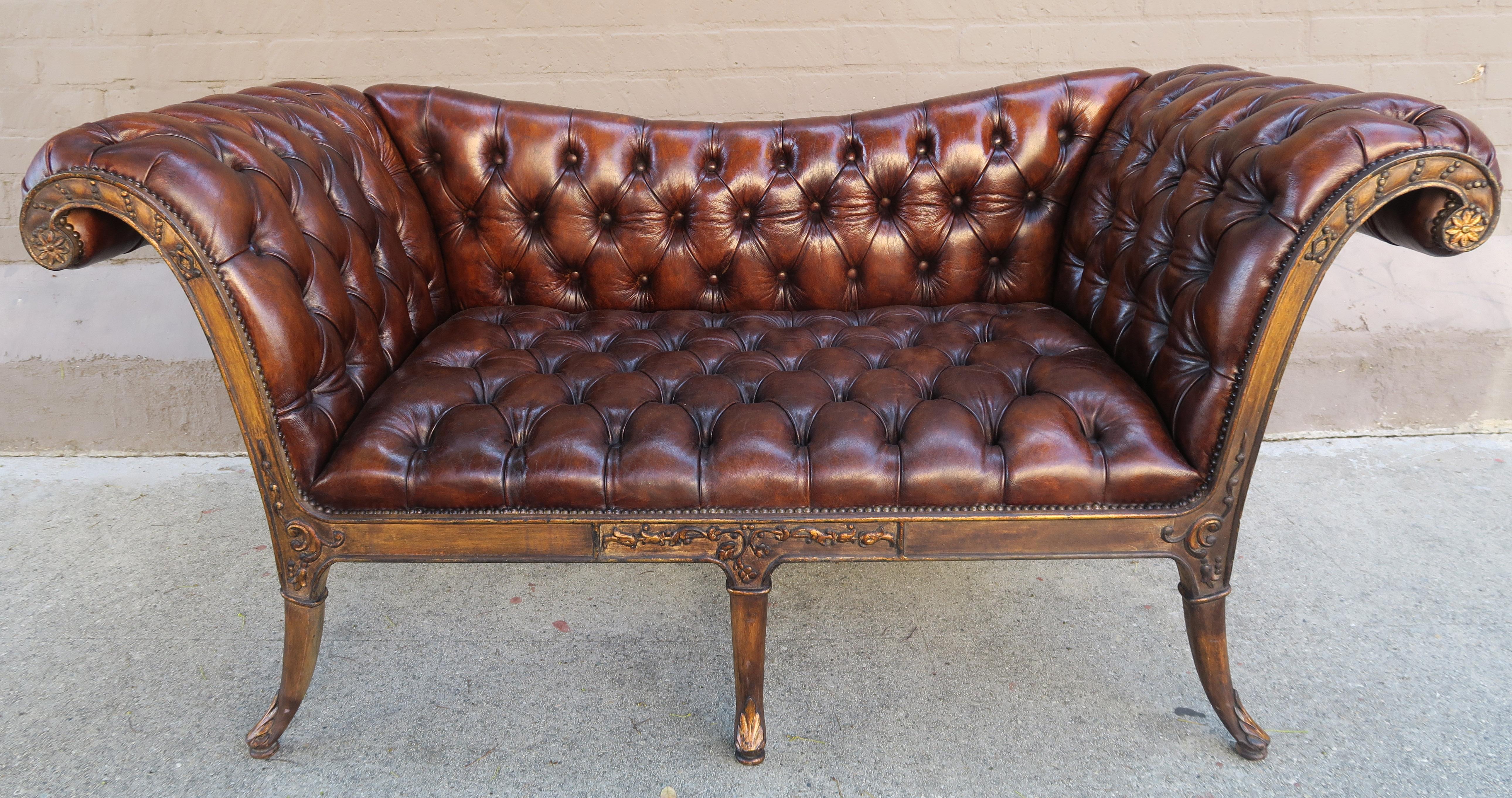 French Regency style carved wood sofa upholstered in tufted beautifully distressed leather and detailed with nailheads. The sofa is finely carved and has parcel gilt detailing. 
Measures: Seat height 18