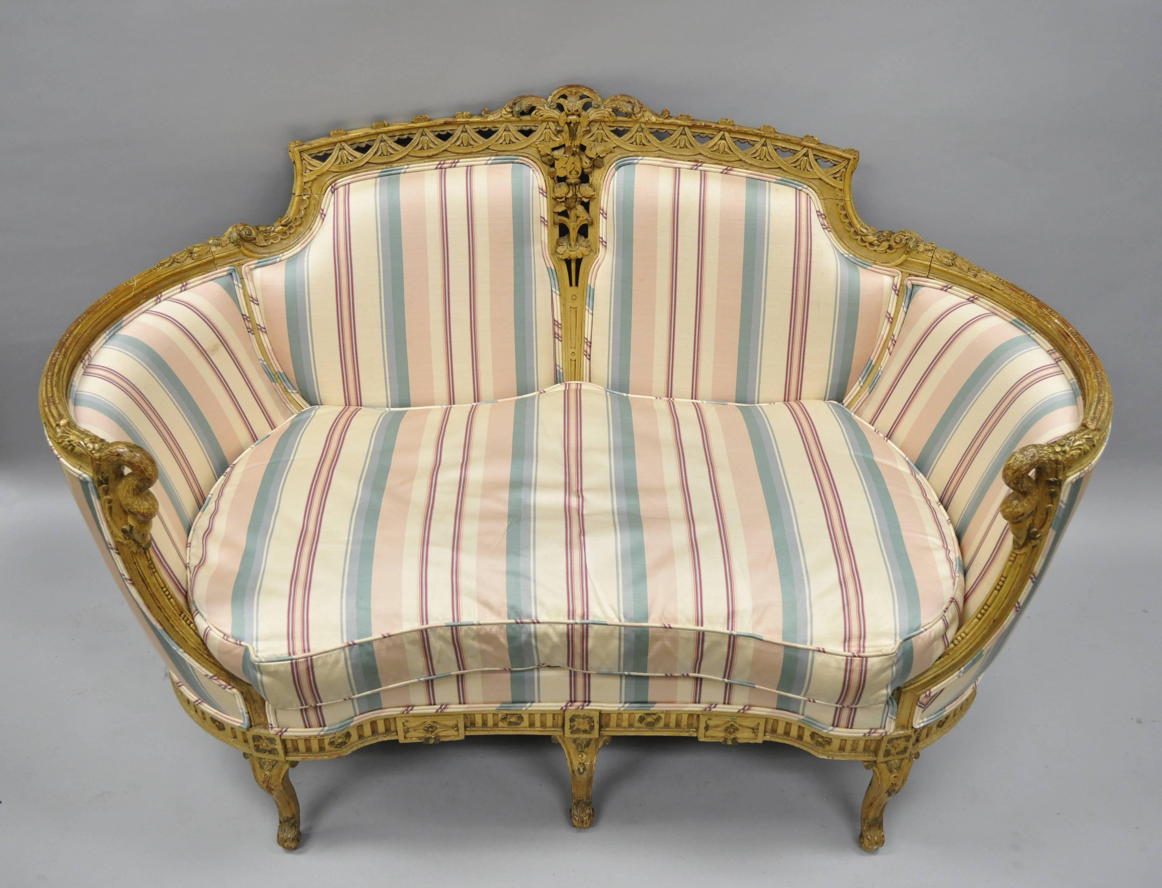 Antique French Regency style swan carved settee. Item features shapely swan carved arms, floral and drape carved backrest, unique oval frame, solid wood construction, cream distress painted finish, seven cabriole legs, and great style and form,