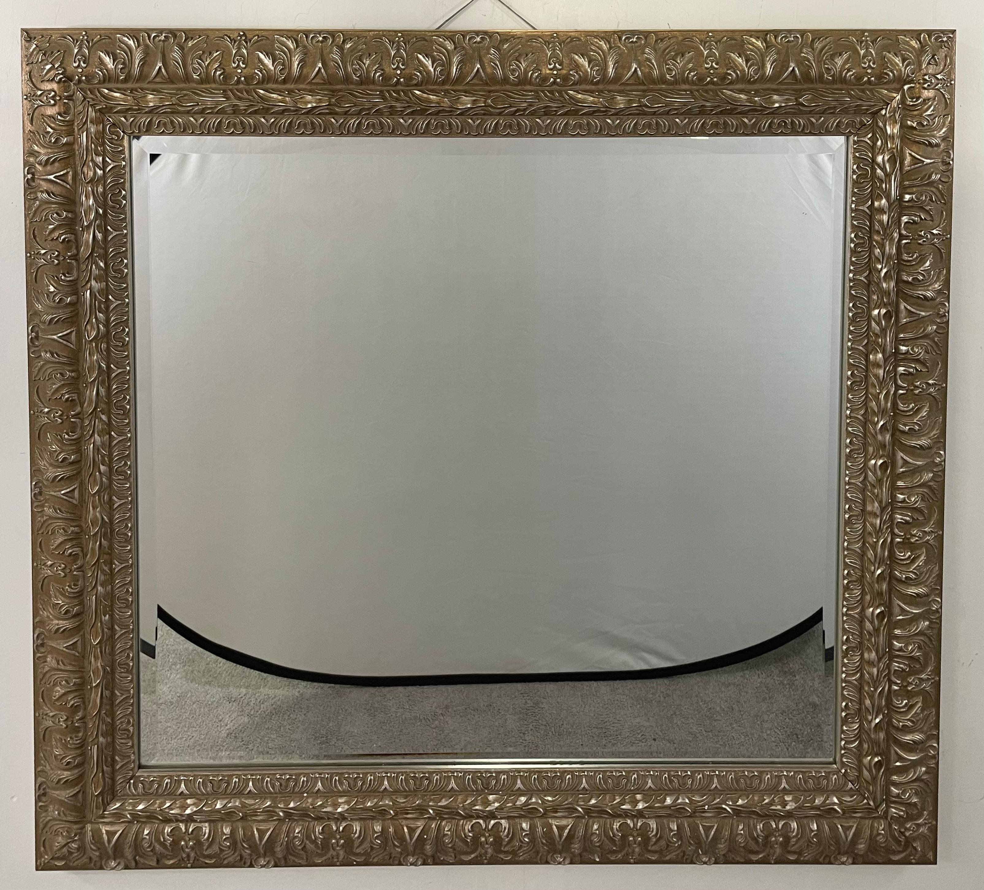 An elegant French Regency style rectangular mirror. The wall or Mantel mirror features detailed hand carving presenting acanthus and leaves motifs all over the frame all made in a silver /champagne color. The beautiful mirror has a beveled glass.
