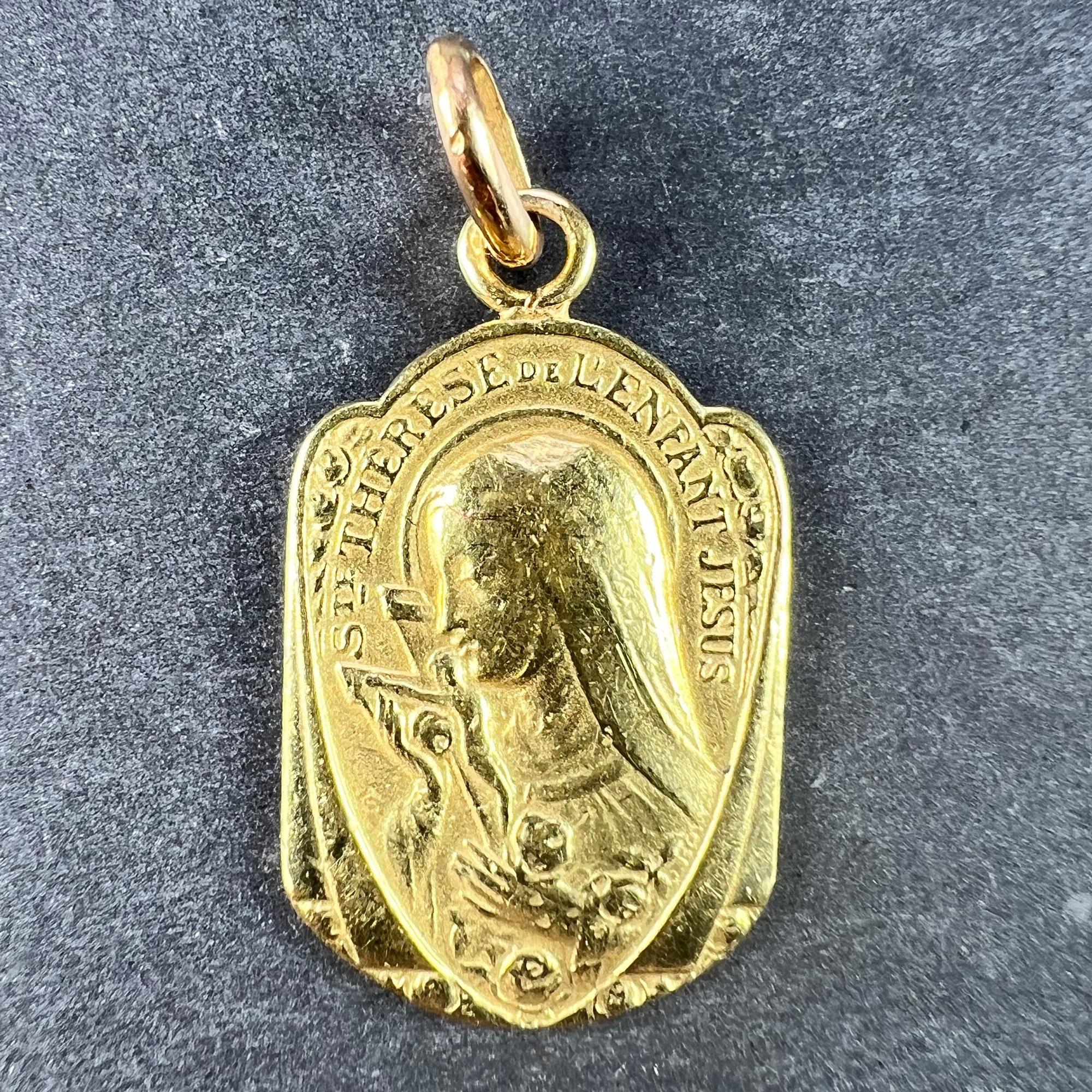 A French 18 karat (18K) yellow gold charm pendant designed as a medal depicting Saint Therese with a halo with the phrase 'ST THERESE DE L'ENFANT JESUS' (Saint Therese of the Infant Jesus) holding a crucifix and some roses, the surround with Art