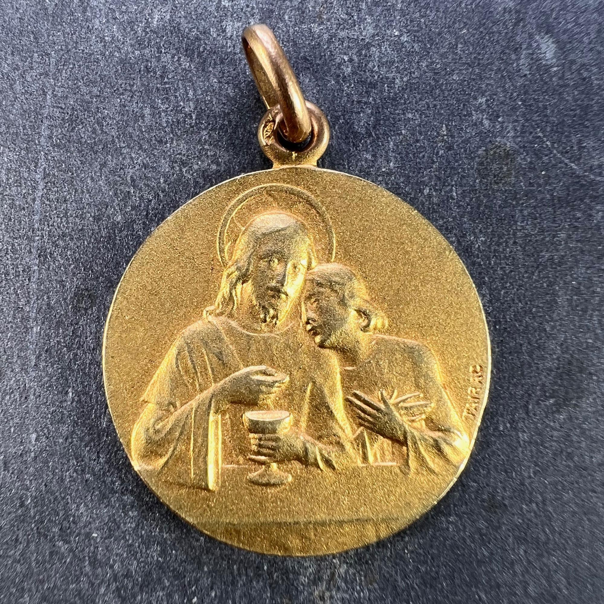 A French 18 karat (18K) yellow gold charm pendant designed as a medal depicting Jesus preparing the holy communion at the Last Supper to one side. The reverse depicting an angel holding a sheaf of lilies, engraved with the monogram LM / ML and the