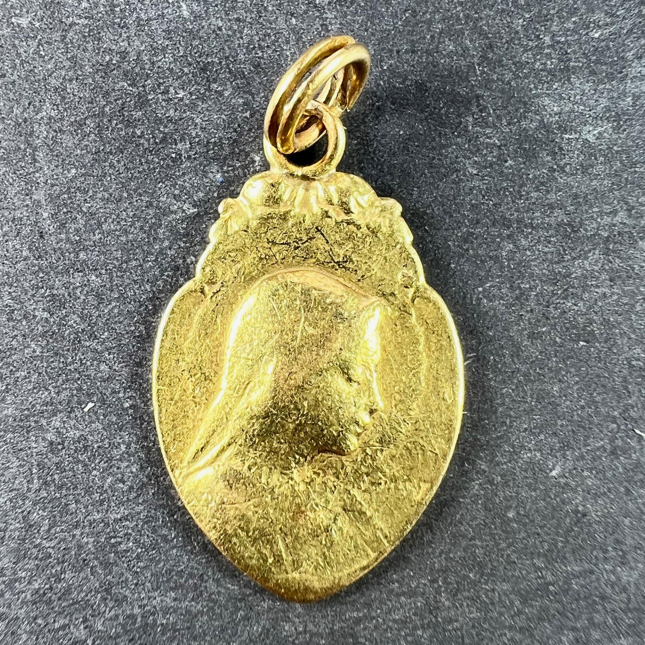 A French 18 karat (18K) yellow gold charm pendant designed as a shield-shaped medal depicting the Virgin Mary backed by a halo and surmounted by roses; engraved with a monogram for CS to the reverse and dated 1er Octobre 1932. Stamped with the