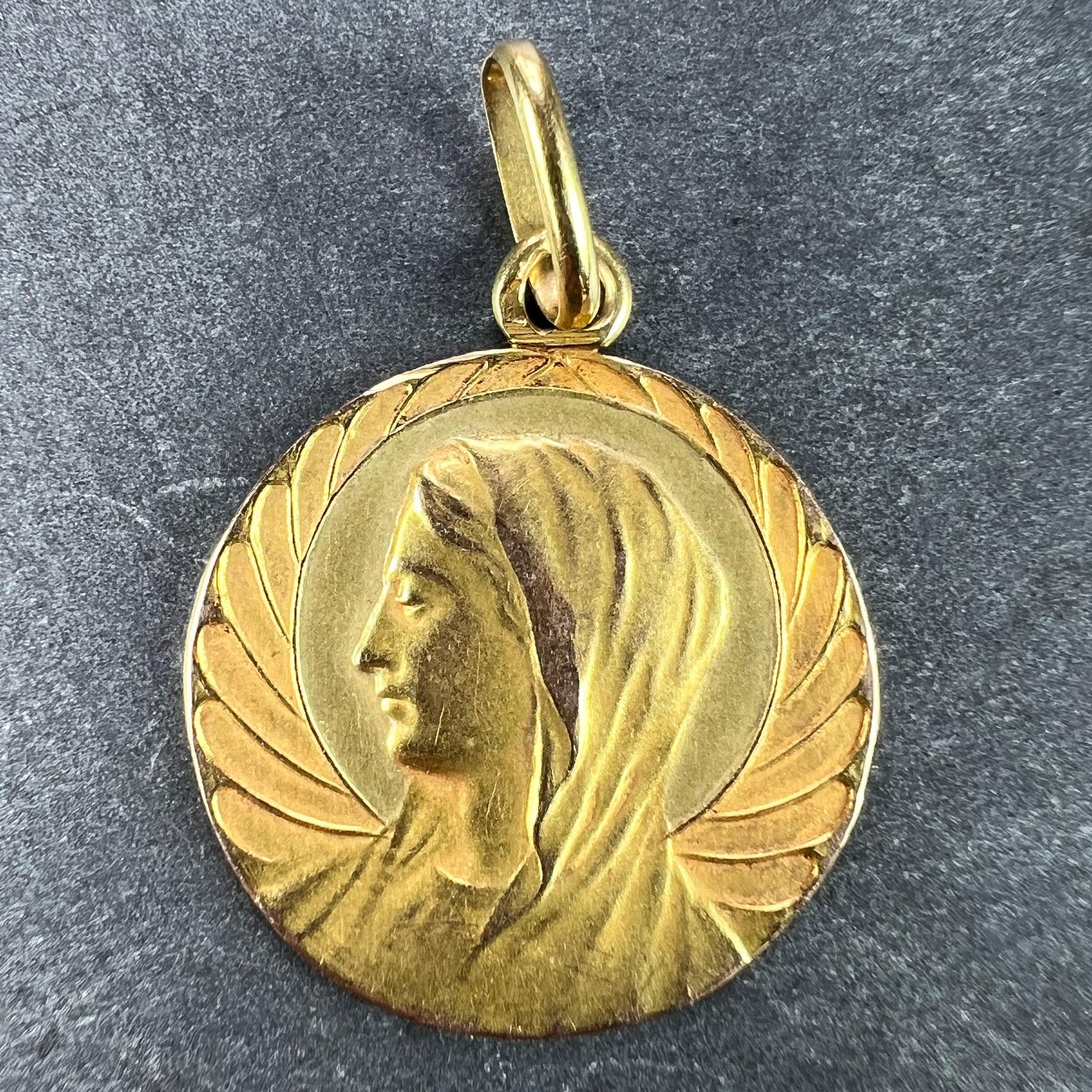 An 18 karat (18K) yellow gold religious charm pendant designed as a medal depicting the Virgin Mary with a halo against a scalloped background resembling angel wings. Stamped with the eagle's head mark for 18 karat gold and French manufacture. The
