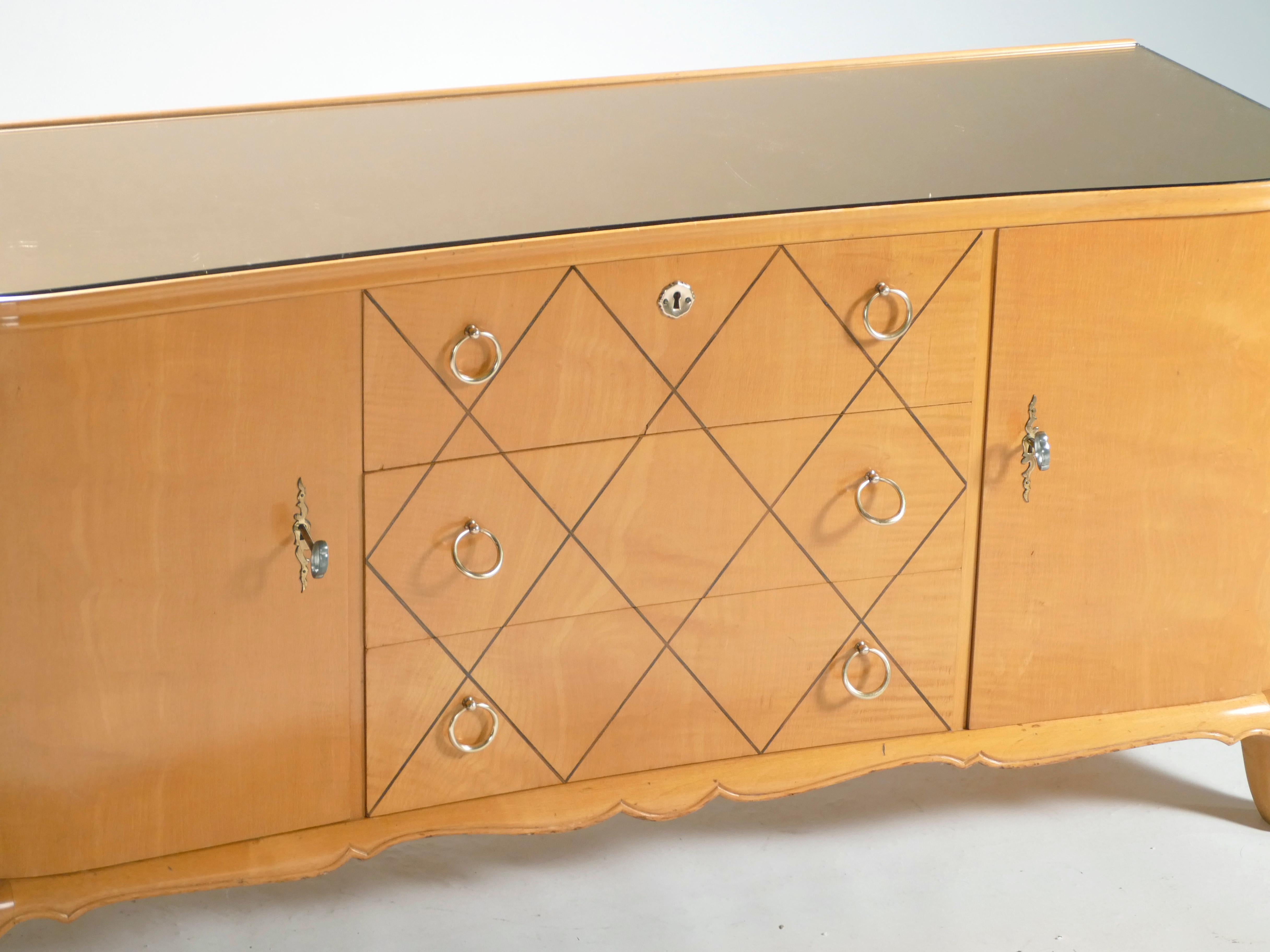 Most likely originally intended for a bedroom, this 1950s chest of drawers or sideboard imparts a cozy, glowing mood to a space. The warm sycamore maple remains looking healthy and smooth 70 years later. Quality bronze rings and accents adorn the