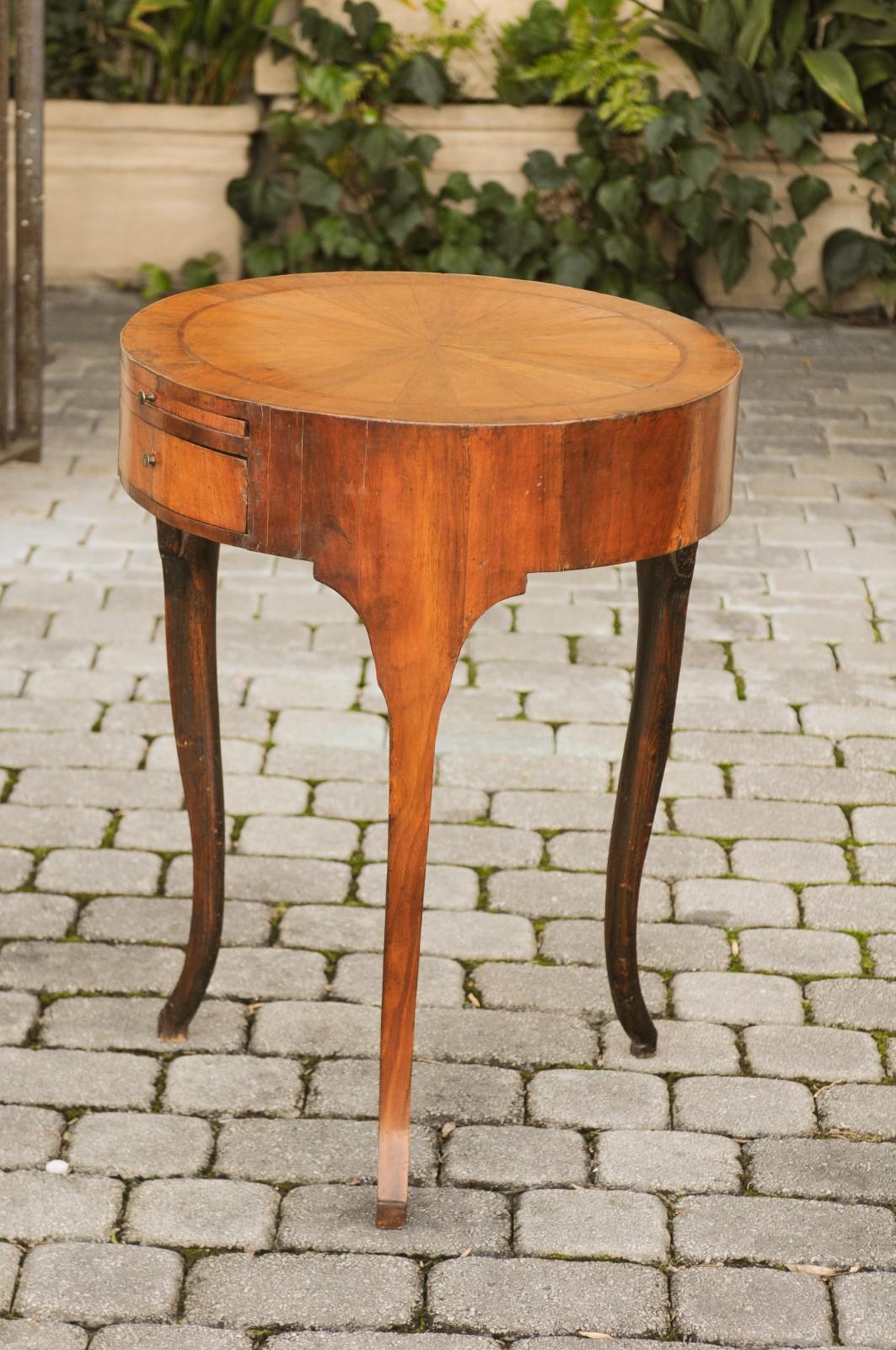 A French Restauration period round walnut side table from the early 19th century, with radiating veneer, drawers and curving legs. Born in the early years of the 19th century during the brief return of monarchy, this French side table features a