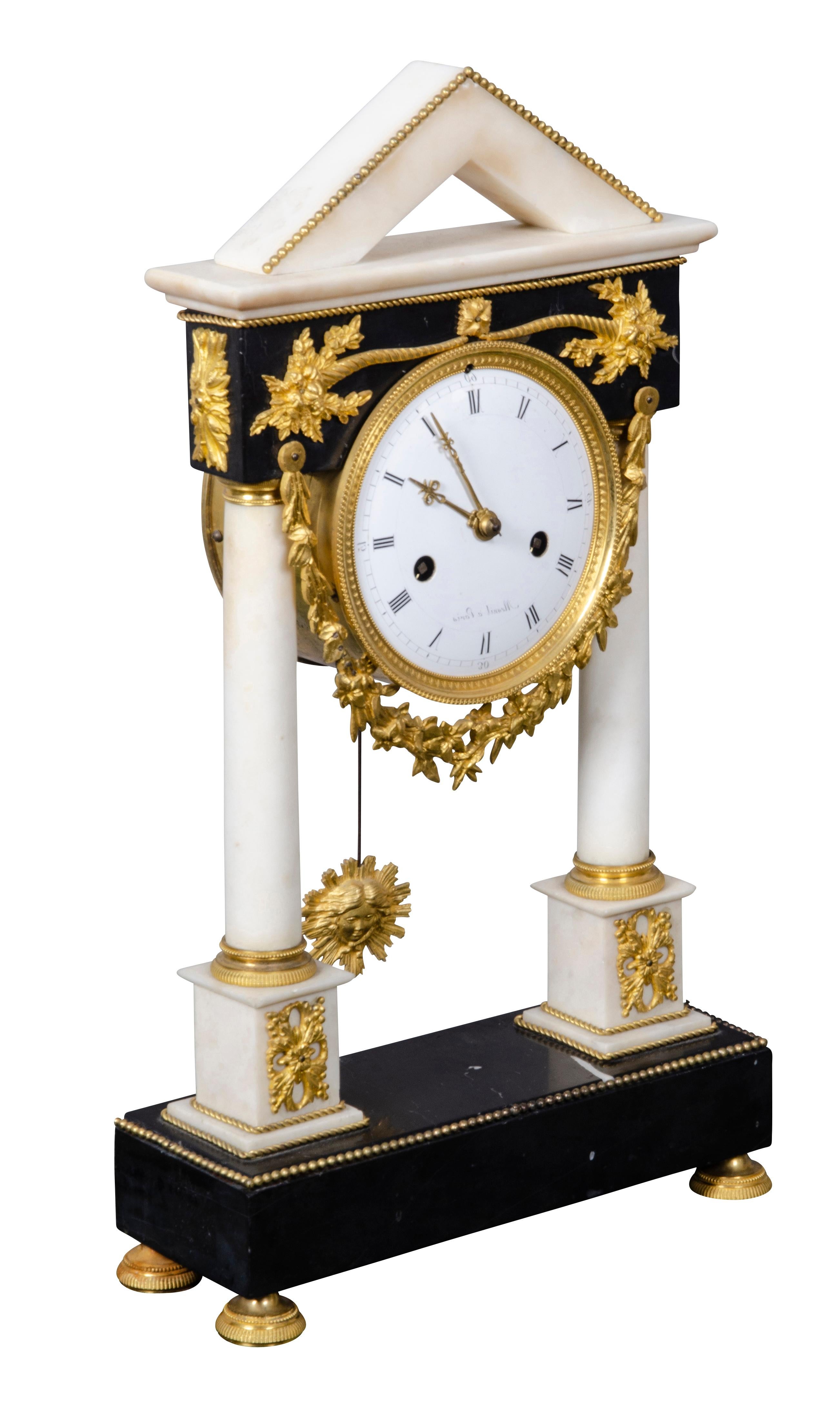 With pointed architectural pediment over an enamel clock face with signature of Mesnil of Paris. With black marble frieze and white marble columns with bronze mounts on a rectangular marble plinth and bun feet.
