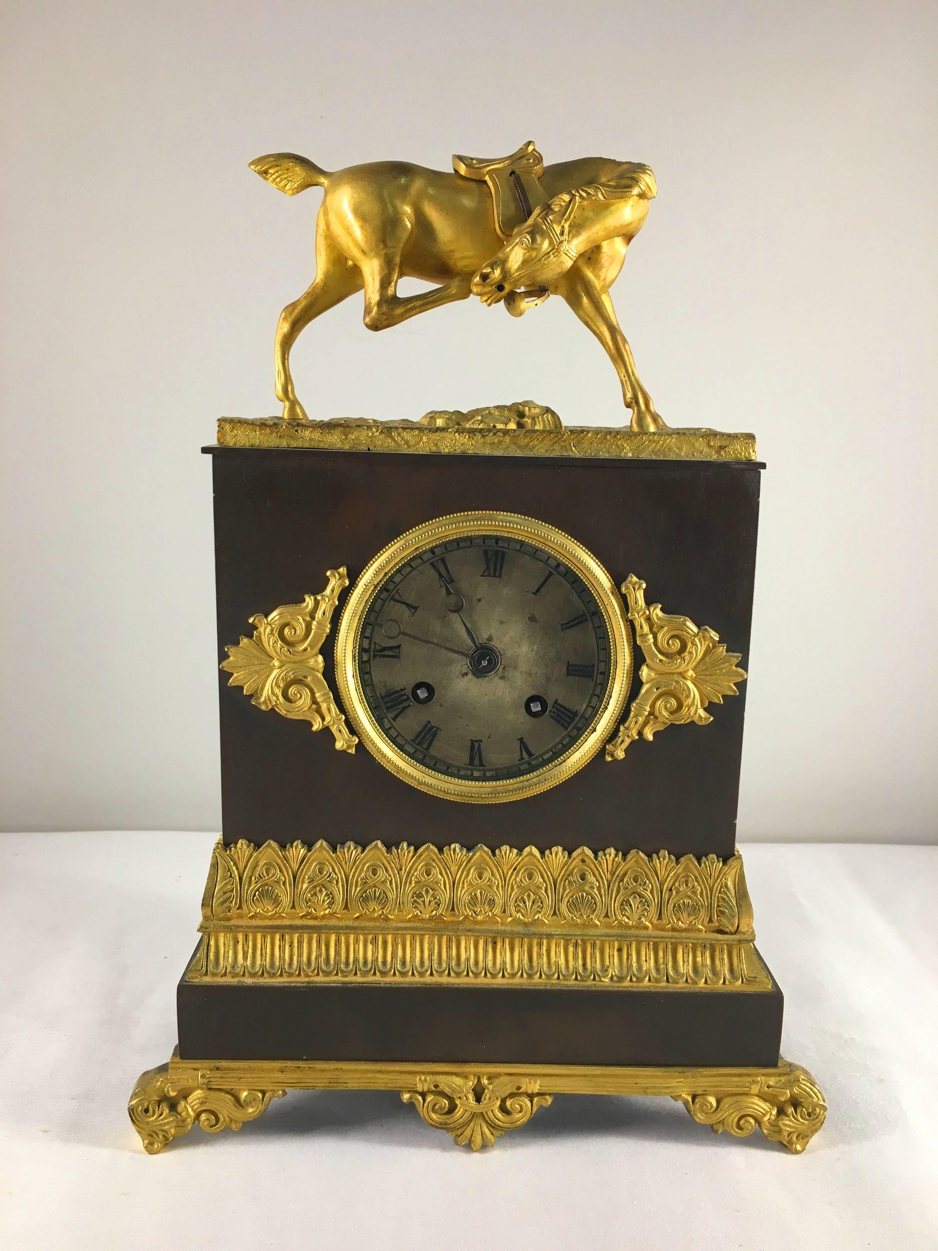 An early 19th century French Restauration period figural mantel clock, the patinated bronze case mounted with gilt bronze decoration, a silvered dial and the top mounted with a gilt bronze horse sculpture. The clock is running and keeps time well,
