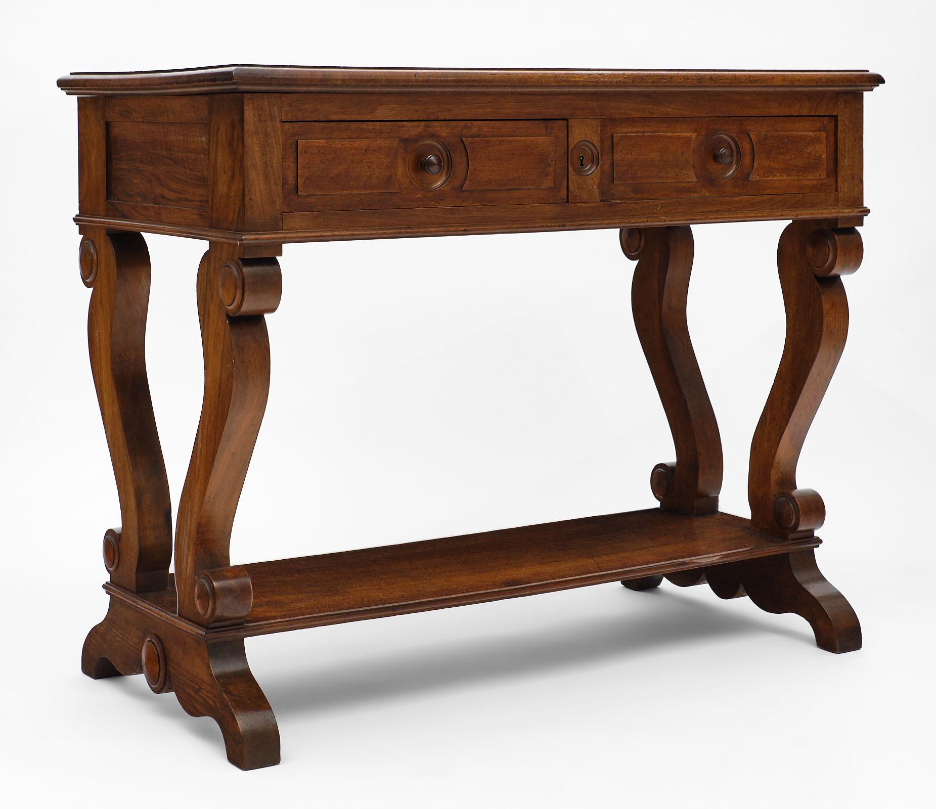 A fine Restoration period French console made of solid walnut and featuring two dovetailed drawers and a bottom shelf. The four console legs are hand carved and support the top, the feet under the shelf are hand carved as well. The piece comes from