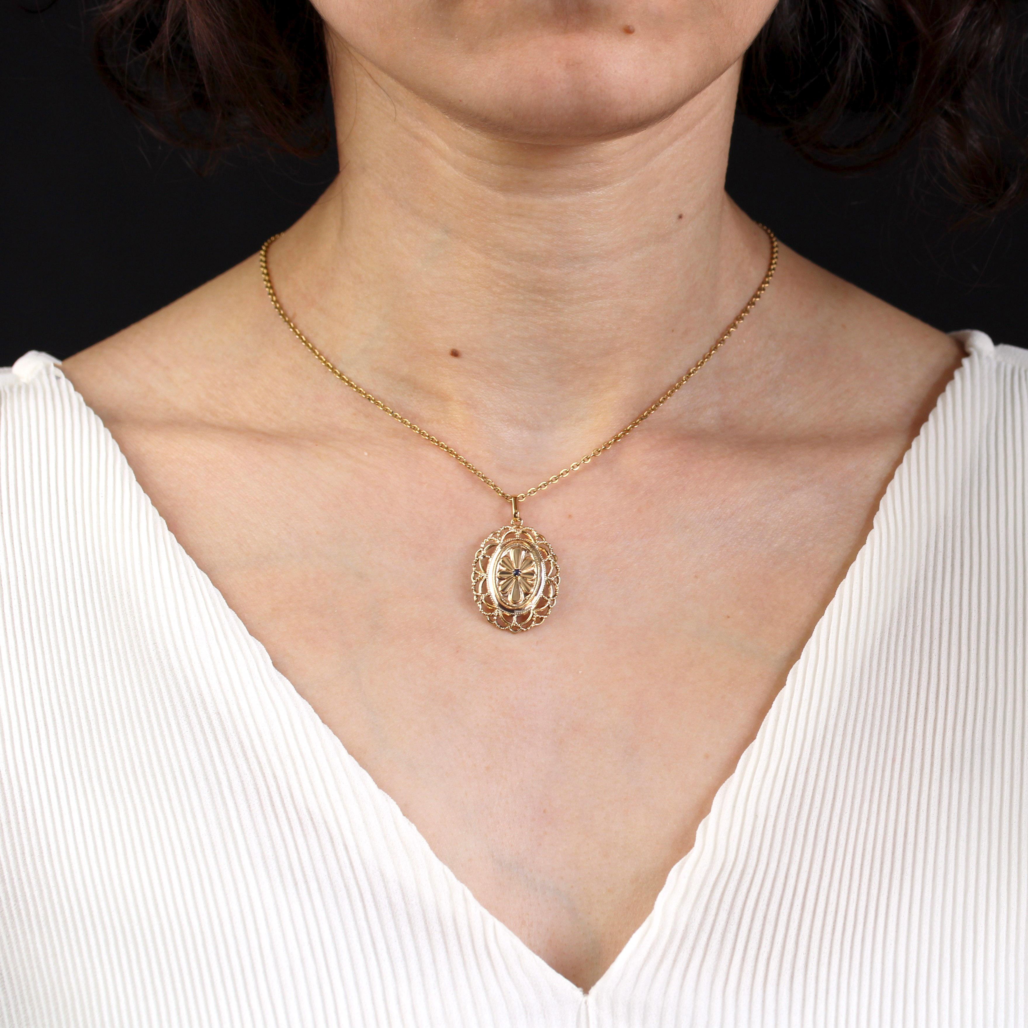 Pendant in 18 karat yellow gold, eagle head hallmark.
A vintage oval pendant features a small, claw-set round sapphire in the center, surrounded by an oval flower motif with striated petals and a chased, pearled edge. The border features openwork
