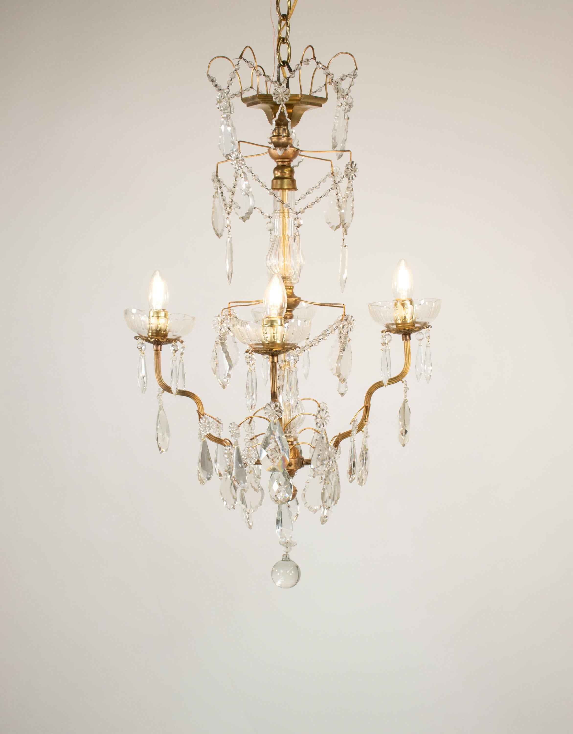 Questo squisito lampadario vintage francese in stile Luigi XV è una testimonianza dell'eleganza e dell'artigianato rococò. Realizzato in ottone, il lampadario presenta quattro bracci ascendenti e delicatamente curvi, ognuno dei quali sostiene una