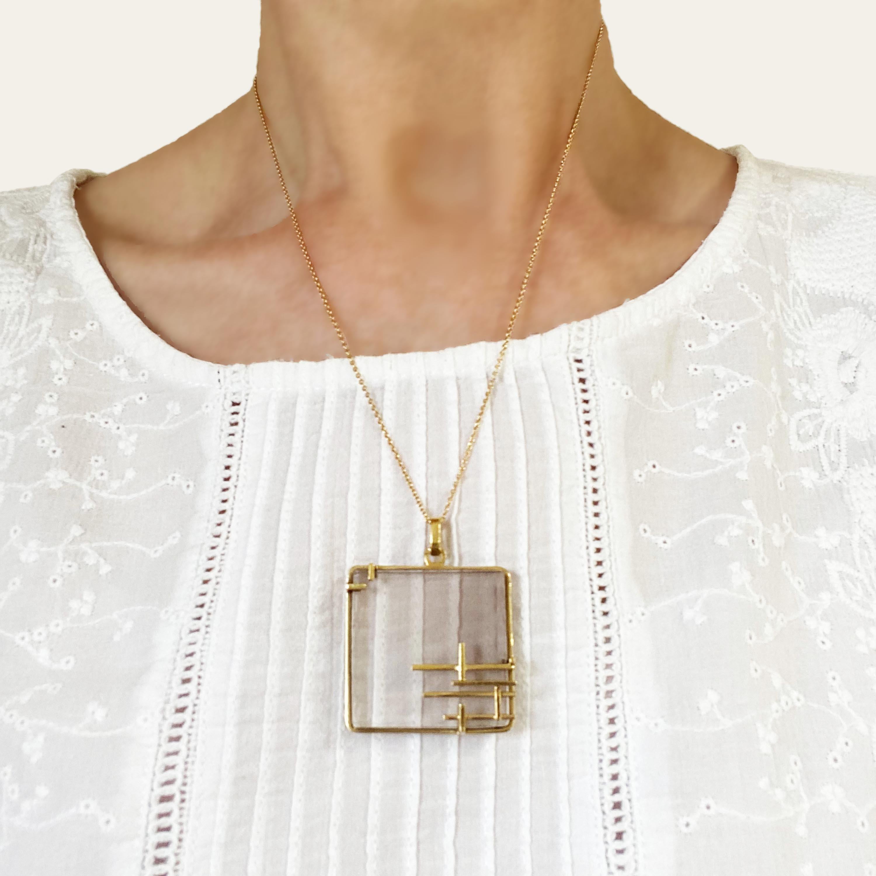 A French retro modernist smoky quartz and gold pendant, with a square, shaded tile of smoky quartz, held by a surround of rectangular heavy gold wire, with abstract, geometric gold, Mondrian influenced, decoration, typical of the period, on a simple
