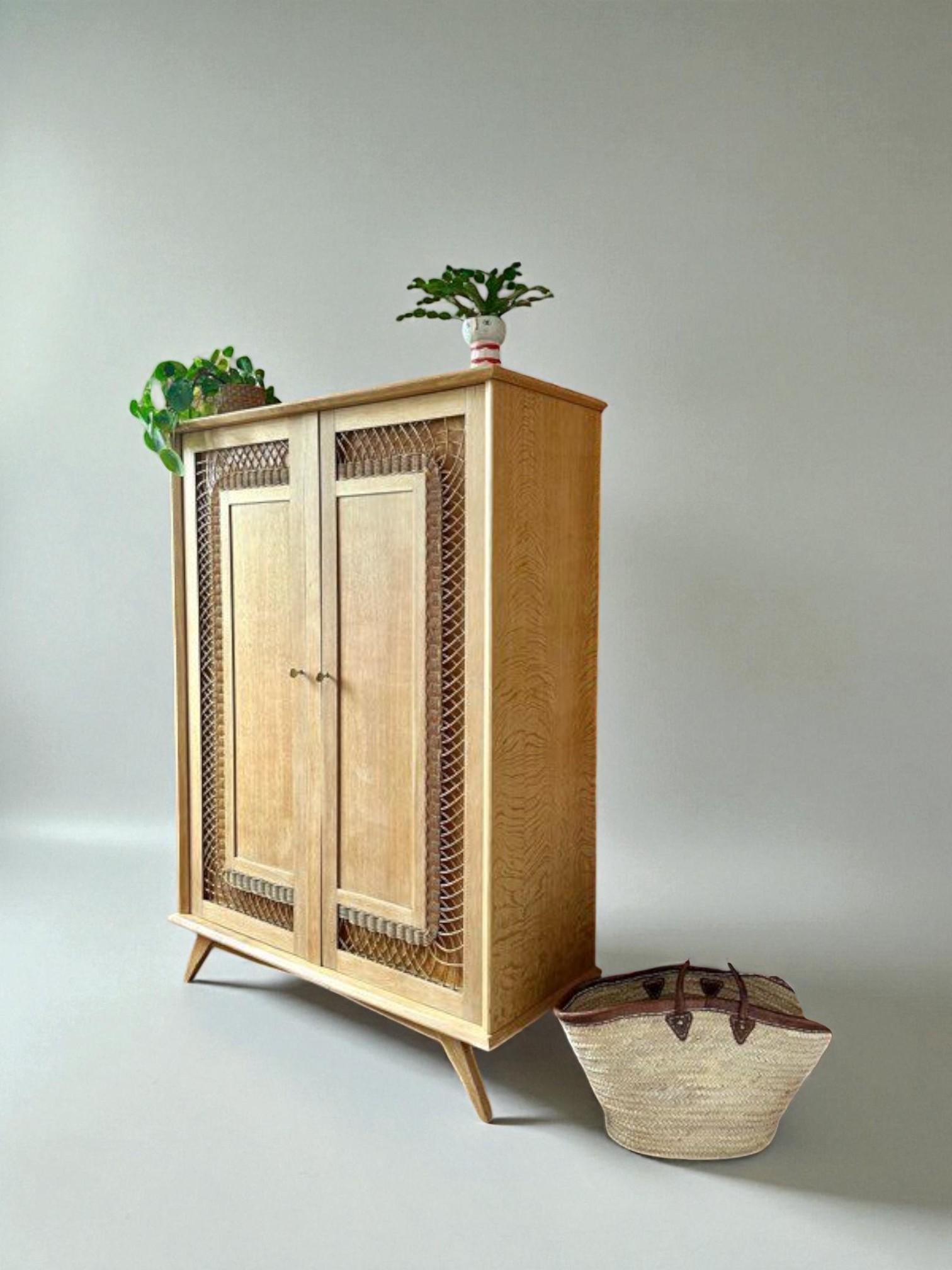 Dieser elegante zweitürige Schrank ist ein unverwechselbares Beispiel für das Design der Jahrhundertmitte, bei dem natürliche Materialien mit geometrischen Details kombiniert werden. Das aus massiver Eiche gefertigte Möbelstück verfügt über große,