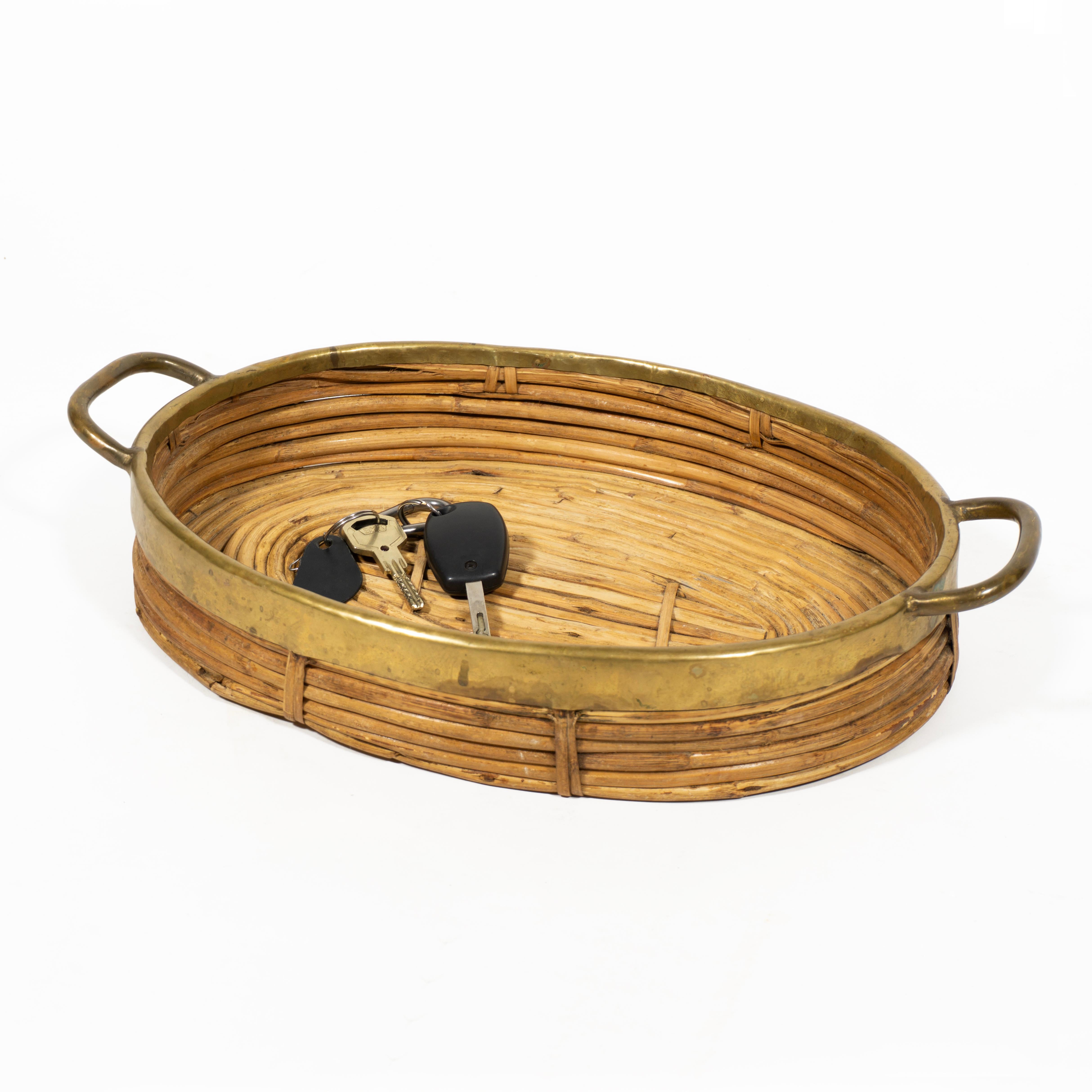 This lovely mid-century modern French Riviera style centerpiece or vide-poche is made of rattan and hand-woven wicker and is complemented by a brass rim and two handles. The tray (in the style of Gabriella Crespi) was designed in Italy during the