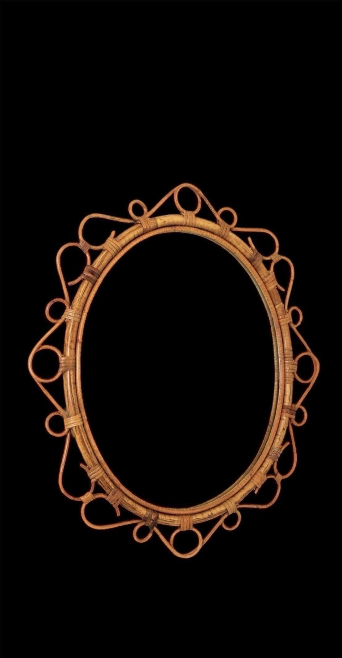 French Riviera oval bamboo and rattan mirror with scrolling detail around the frame. Mediterranean, circa 1960s. 

This Mediterranean wall mirror features an oval bamboo frame surrounded by rattan scrolls and graceful circular decorations. It would