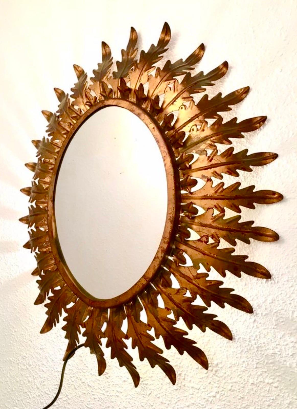 French Riviera oval gold metal mirror with light palm detail around the frame. Mediterranean, circa 1960s. 

This Mediterranean wall mirror features an oval gold metal frame surrounded by scrolls and graceful circular decorations. It would be a new