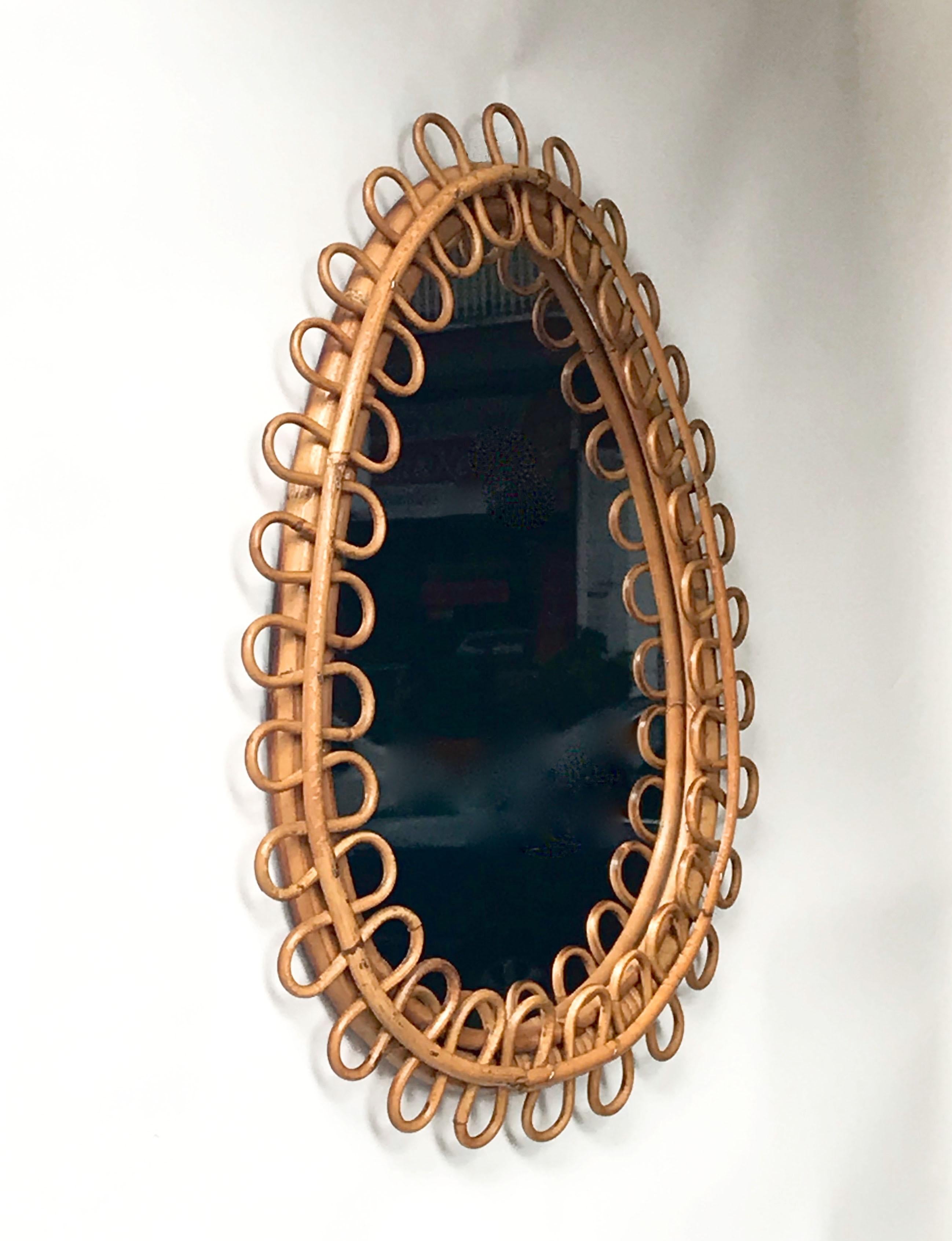 Midcentury decorative oval mirror with curved rattan beams and bamboo frame. This marvellous item was made in Italy during the 1950s.

This piece is unique as it has a sinusoidal rattan frame adding fine and elegant lines to its drop-shaped