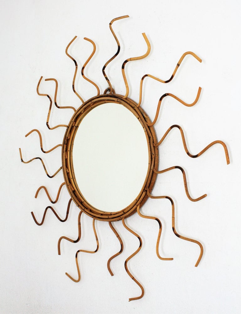 Handcrafted Mediterranean rattan / wicker sunburst with curly rays adorned by pyrography details, France, 1960s.
This mirror has an unusual design with undulating rays. The frame surrounding the glass is made combining alternating curly short and