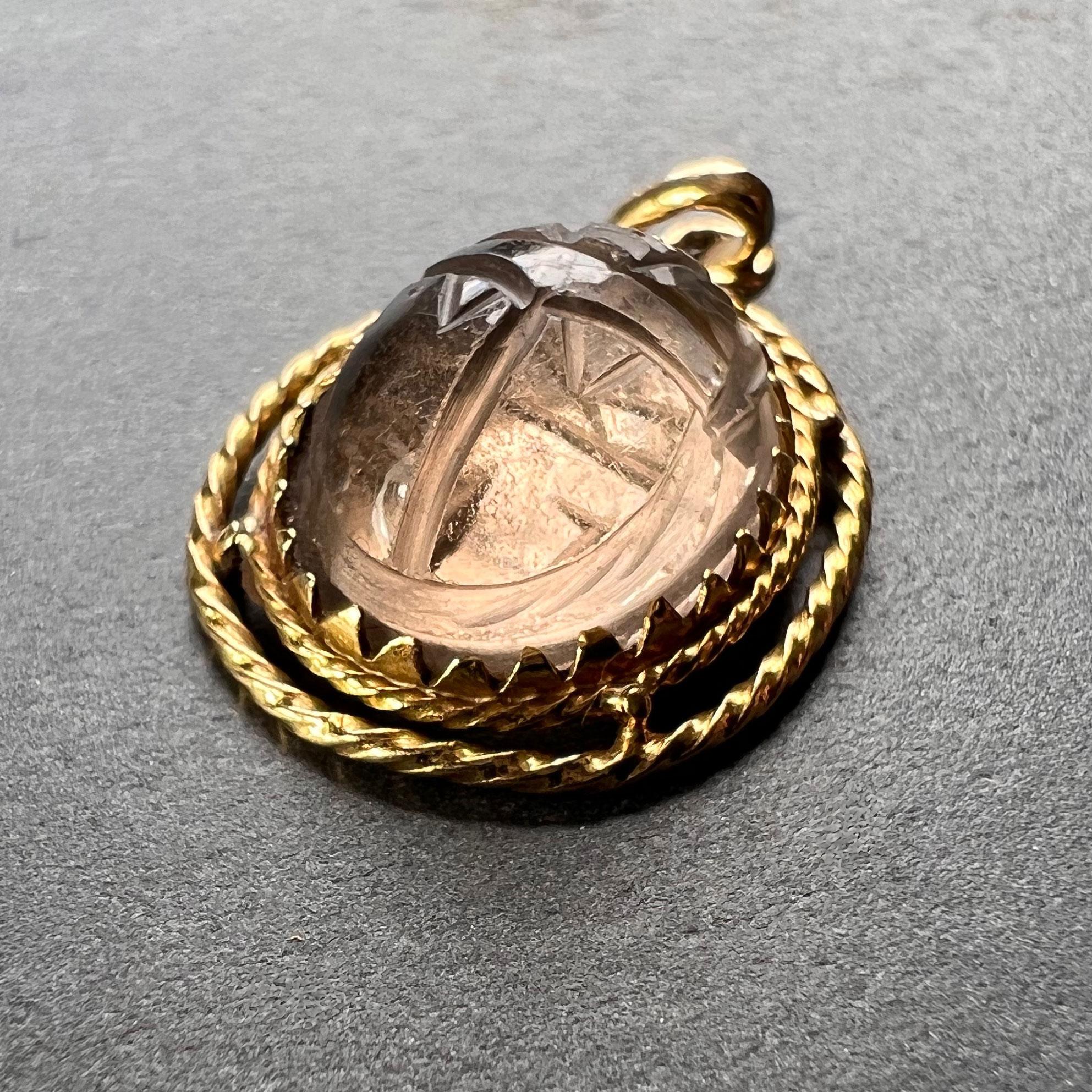 An 18 karat (18K) yellow gold charm pendant designed as the protective amulet of an Egyptian scarab in rock crystal quartz, engraved to both sides and encircled with twisted gold wire. Stamped with the eagle mark for 18 karat gold and French