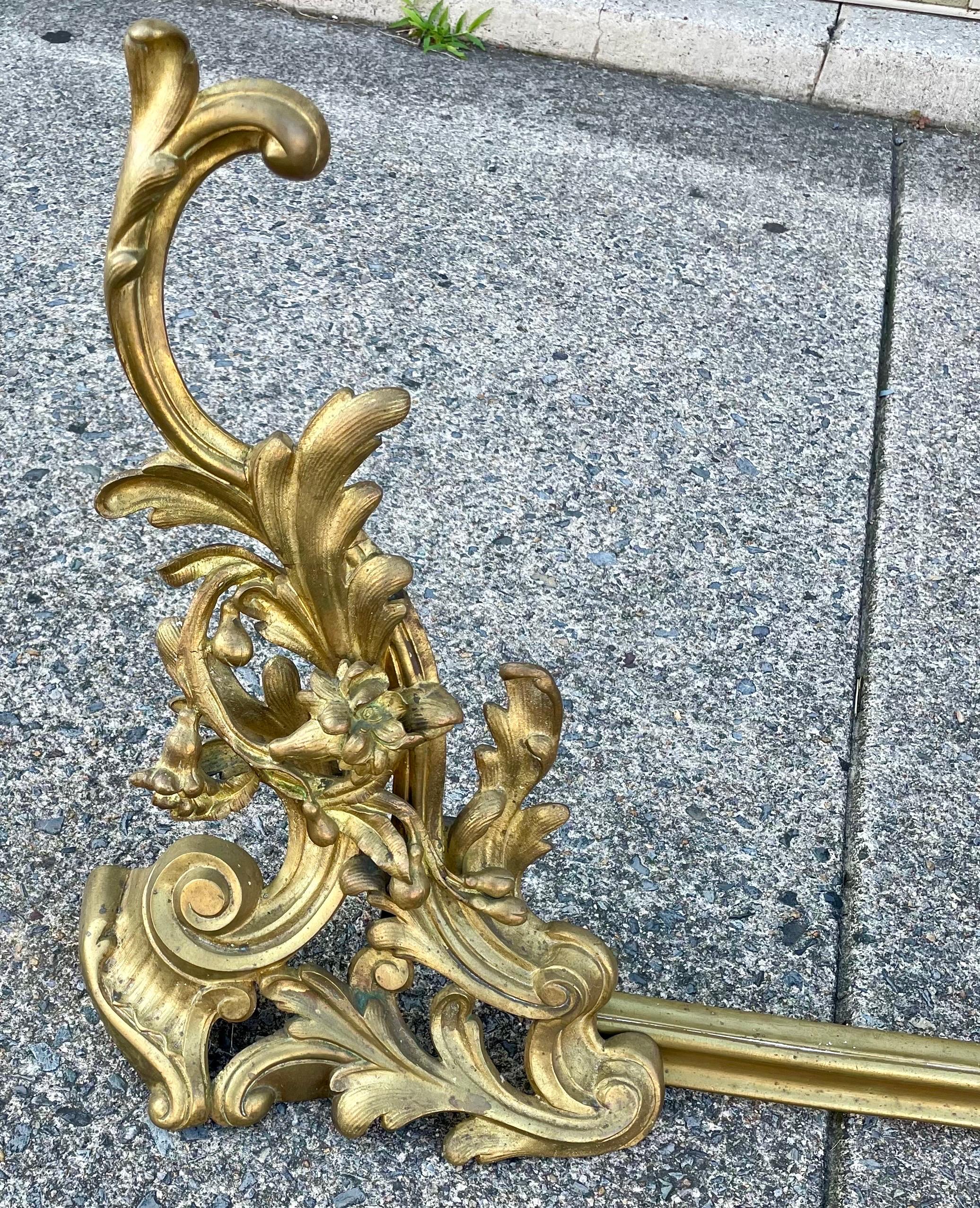 Very sweet pair of brass fireplace chenets or andirons in a rococo style swirl and flower pattern with a fender that is not attached and has a coordinating pattern in it's center. The pair of chenets can be used with or without the fender and with
