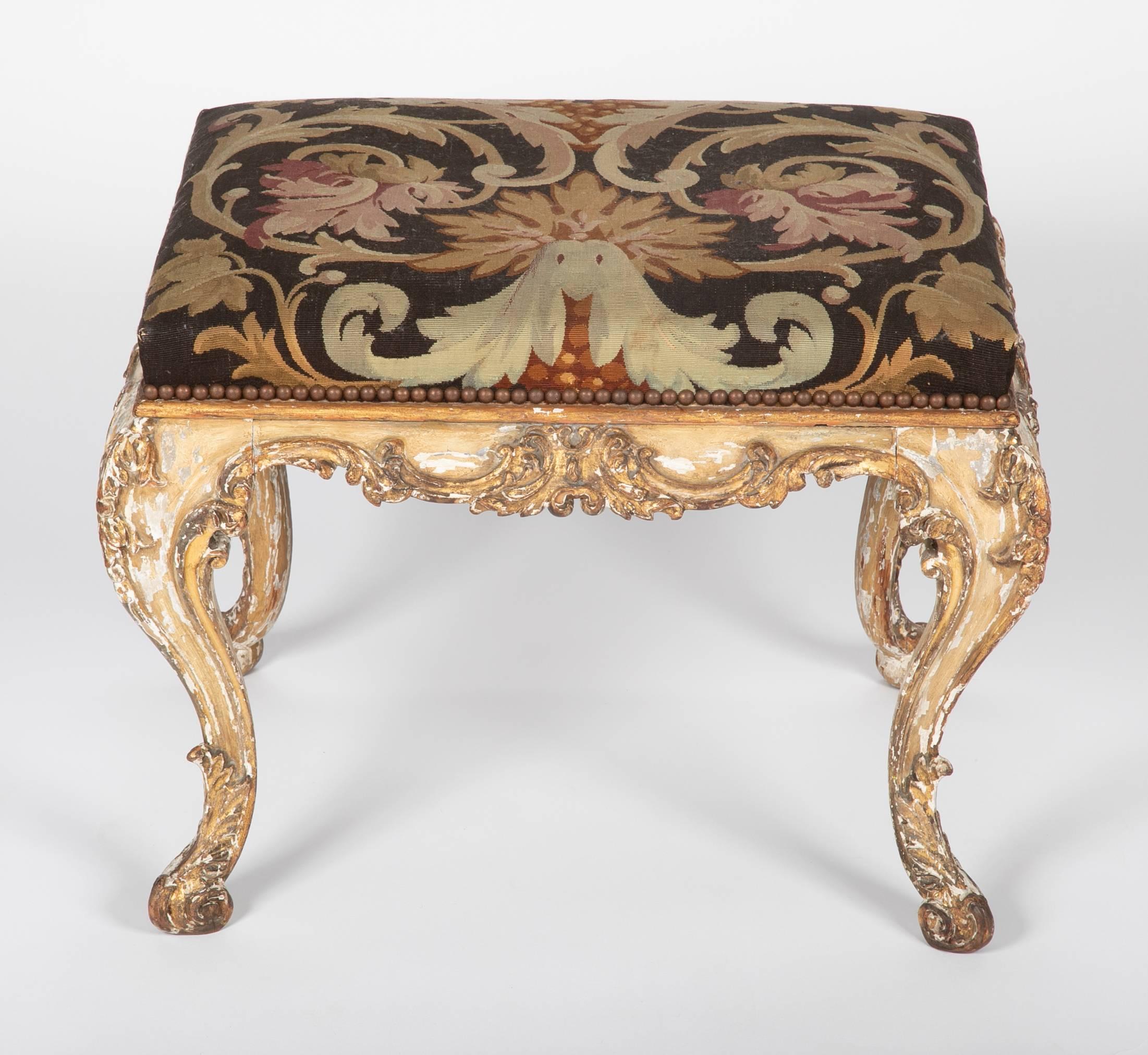 A fine Louis XV style French painted and gilt stool with Aubusson upholstery with brass tacks. On four cabriole legs with raised Rococo gilded carving over a cream colored paint. A very handsome piece. Very nice scale at almost 2 feet wide. (23 w by
