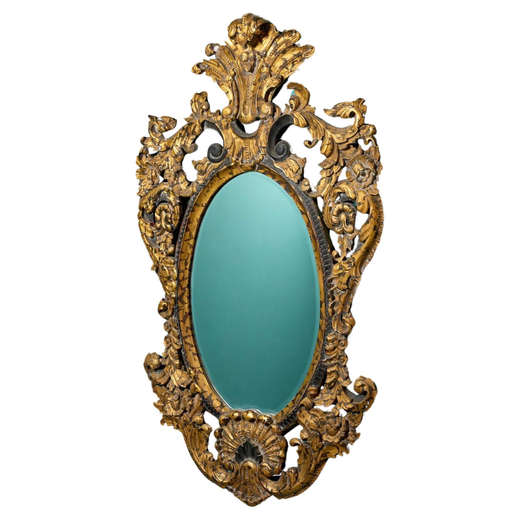 A large and elaborate French rococo style parcel gilt oval wall mirror circa 1900. This striking mirror is an eye-catching feature for an interior wall, extravagantly carved in walnut with scrolling foliage, acanthus crest and parcel gilded in a