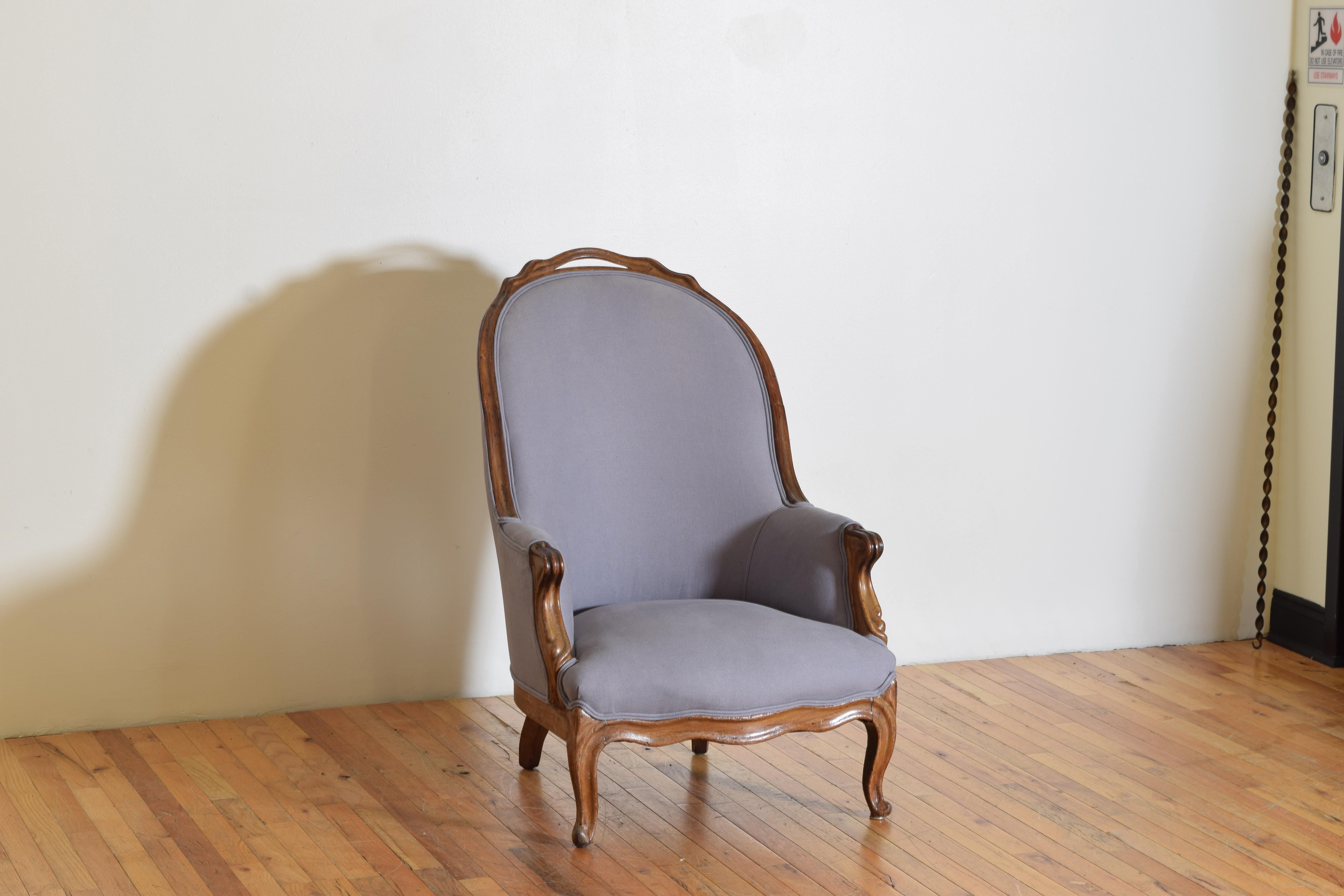 Having an arched and deep set backrest with a carved handle with enclosed sides and carved armrests, the tight seat raised on cabriole legs.