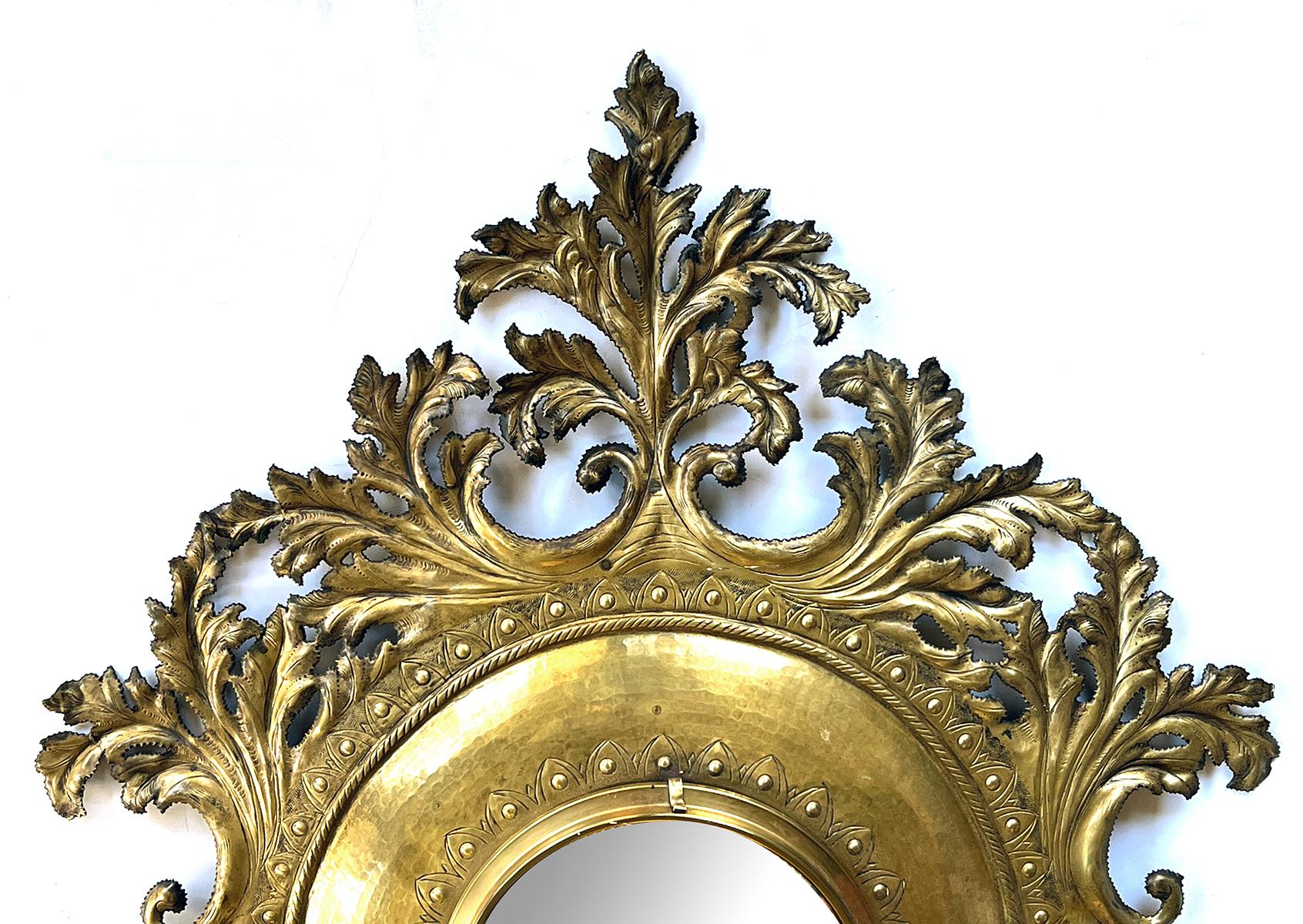 Centering a convex mirror within a brass frame surrounded by lively cut brass foliage.