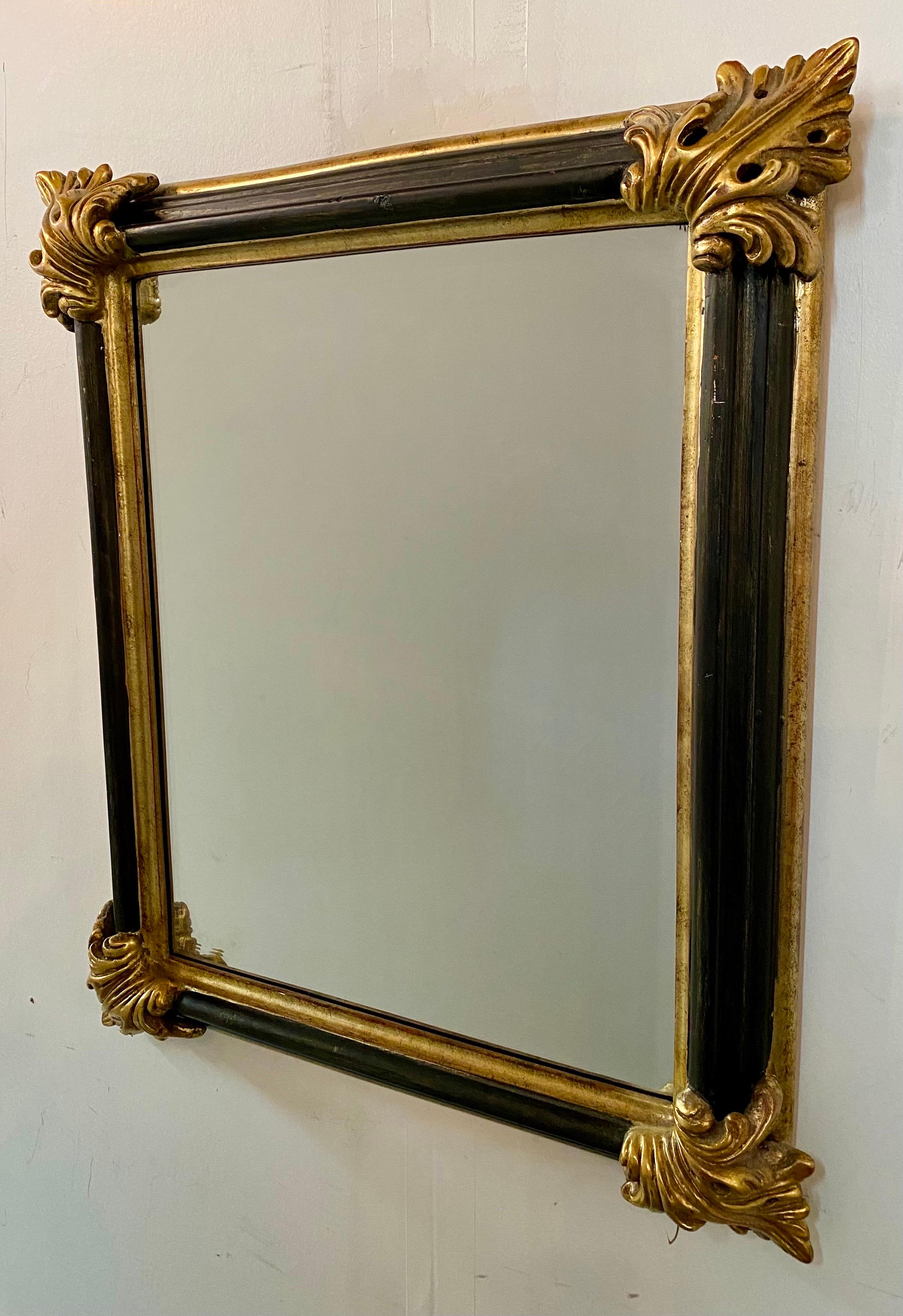 An elegant French Rococo style rectangular mirror. The sturdy and well made mirror features ebony black frame embellished with gold gilt. Each corner shows a large gold leaf design adding style to the piece. Simple with a subtle opulence, the hand-
