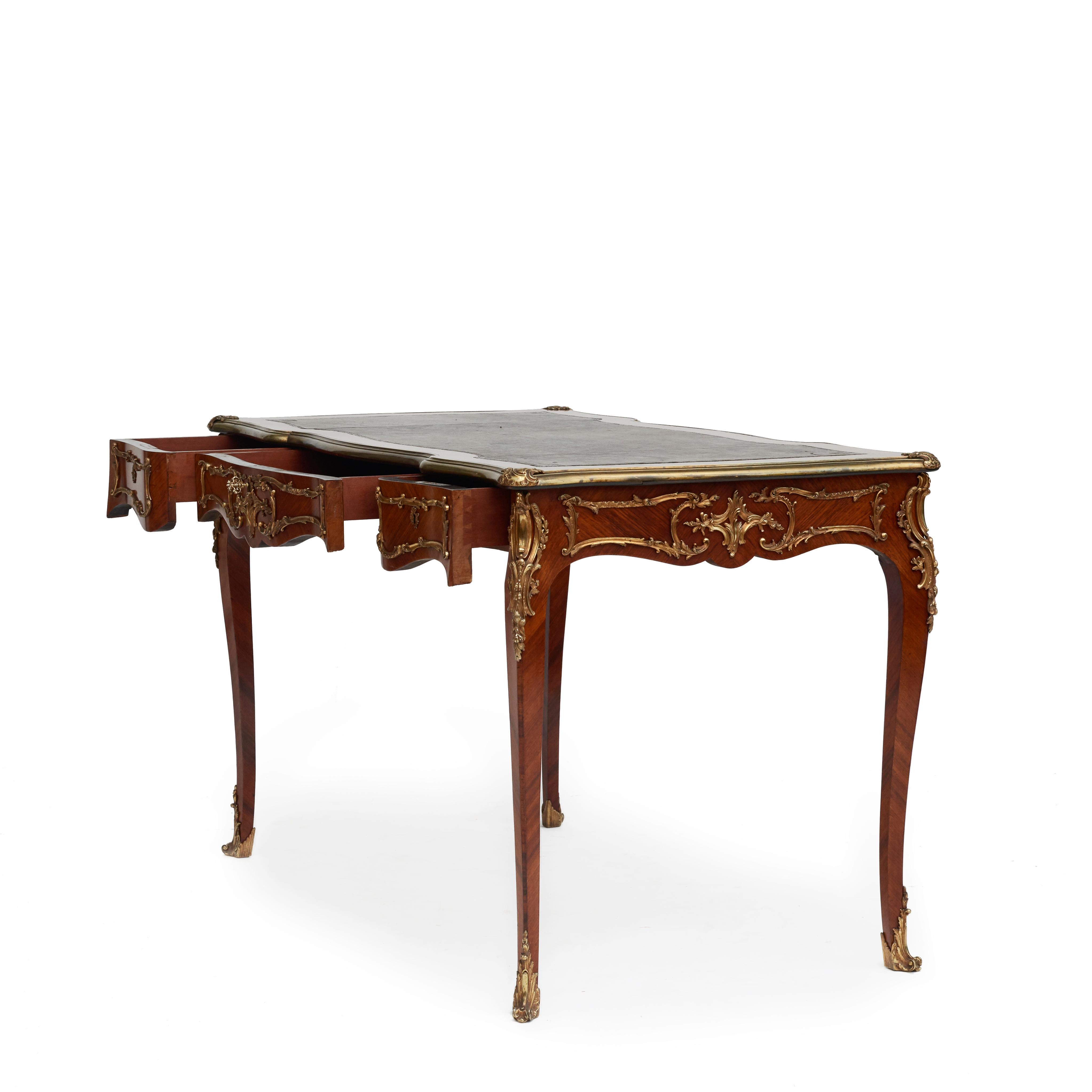 An elegant French rococo style bureau plat writing desk made in walnut with ormolu accents.
Features a top with a tooled leather writing-surface within a walnut border with a serpentine bronze edge and mounts to the corners.
Three drawers to the