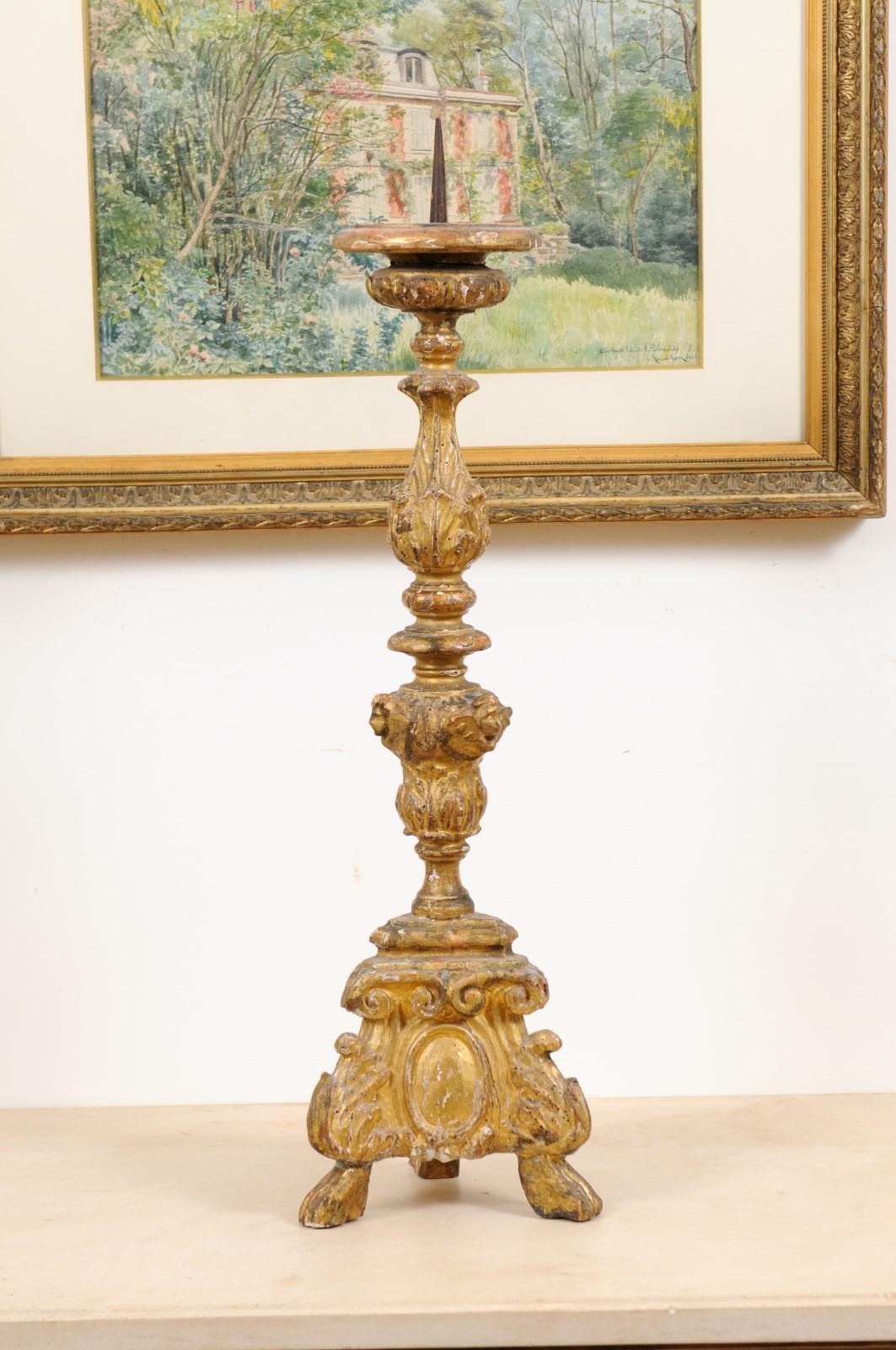 A French Rococo style carved giltwood candlestick from the 19th century, with tripod base and paw feet. Created in France during the 19th century, this Rococo style candlestick features a central carved column adorned with well worn angel faces and