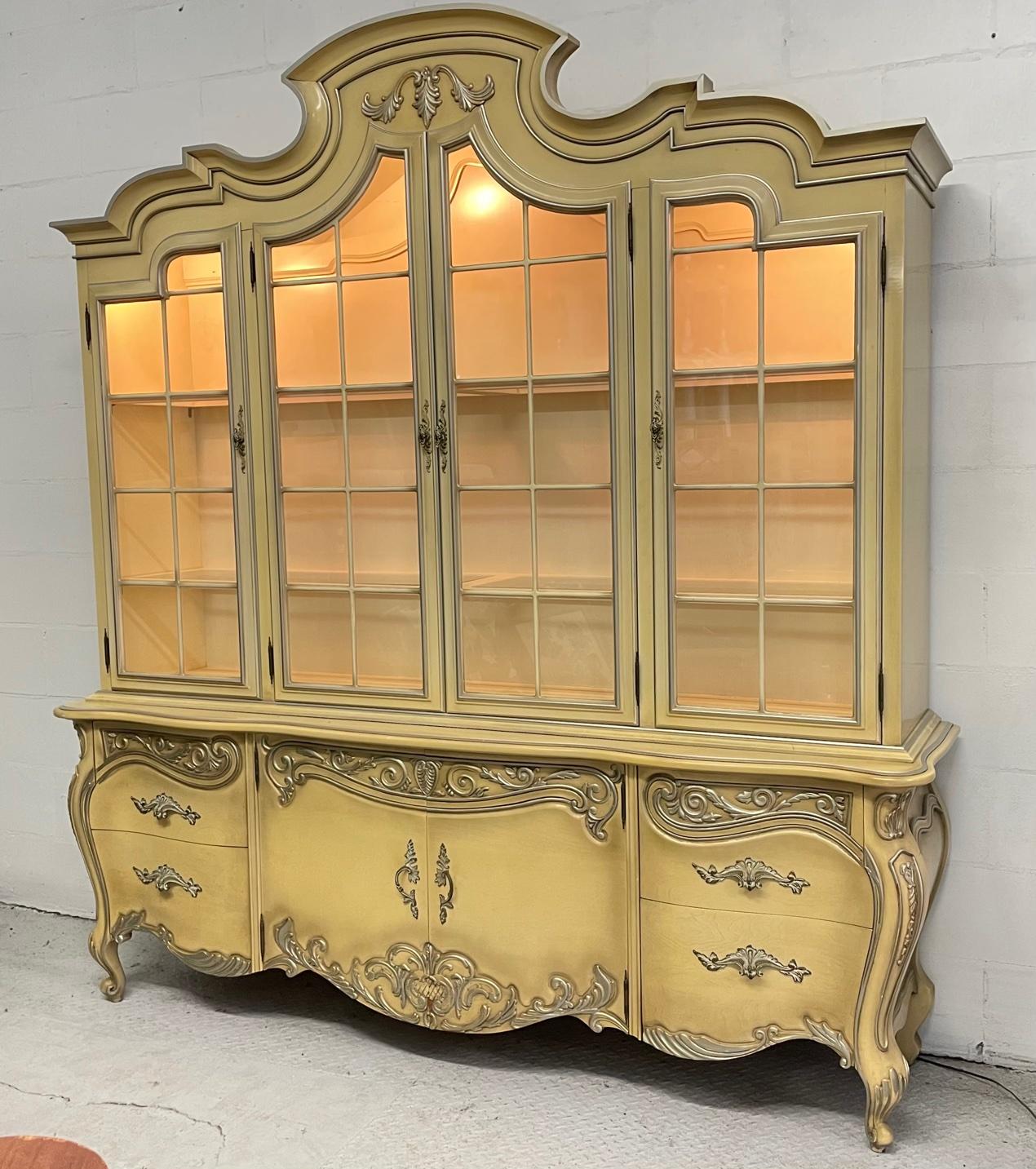 Large lighted dining cabinet by Romweber in ornate French Rococo style features lighted interior and onlays of cartouche design elements. Good condition with minor imperfections consistent with age.