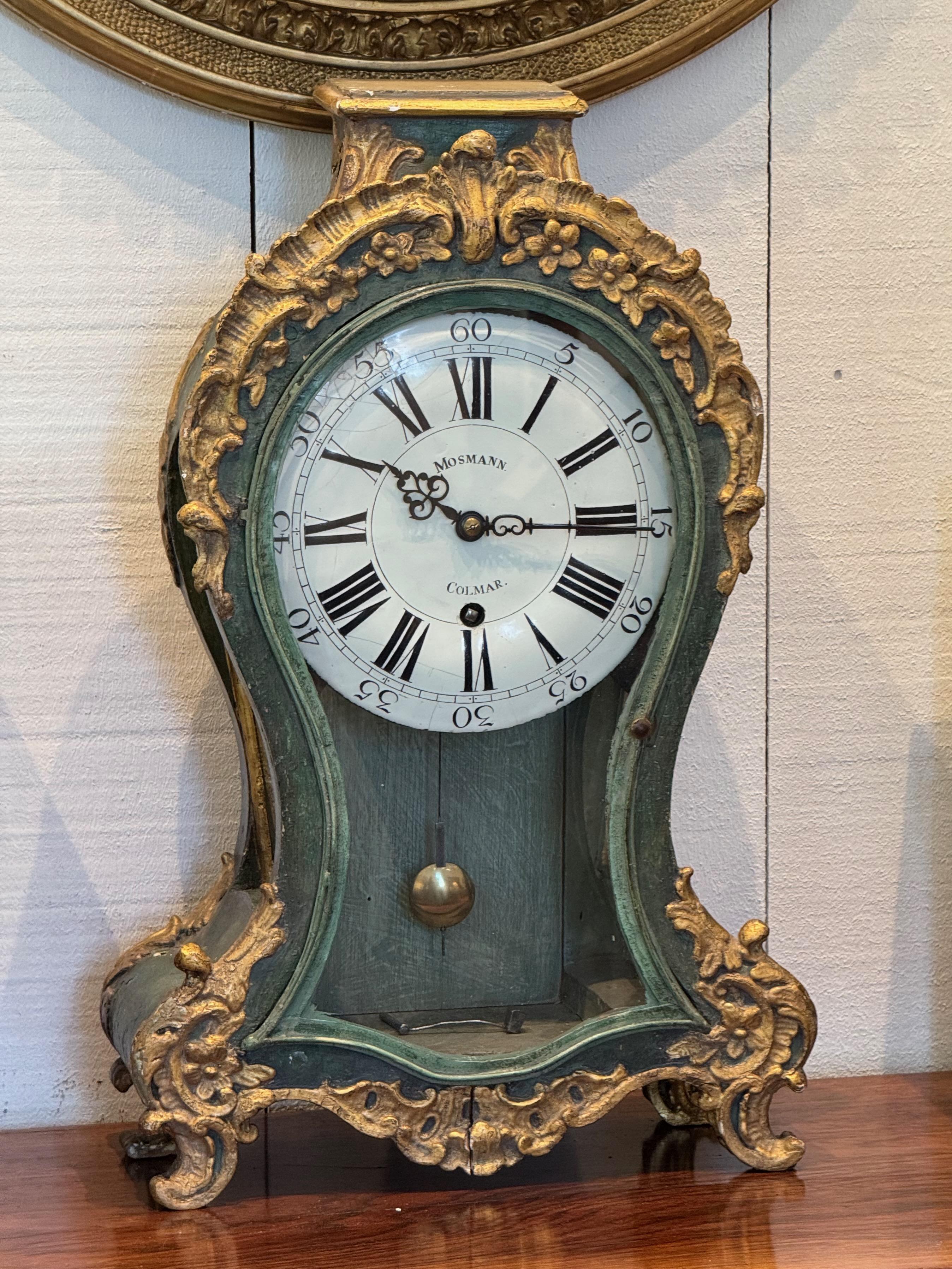Reloj decorativo francés de sobremesa con caja de madera dorada y con roleos, de estilo rococó. El acabado verde pintado se acentúa con detalles florales y foliados dorados. La esfera esmaltada está firmada 