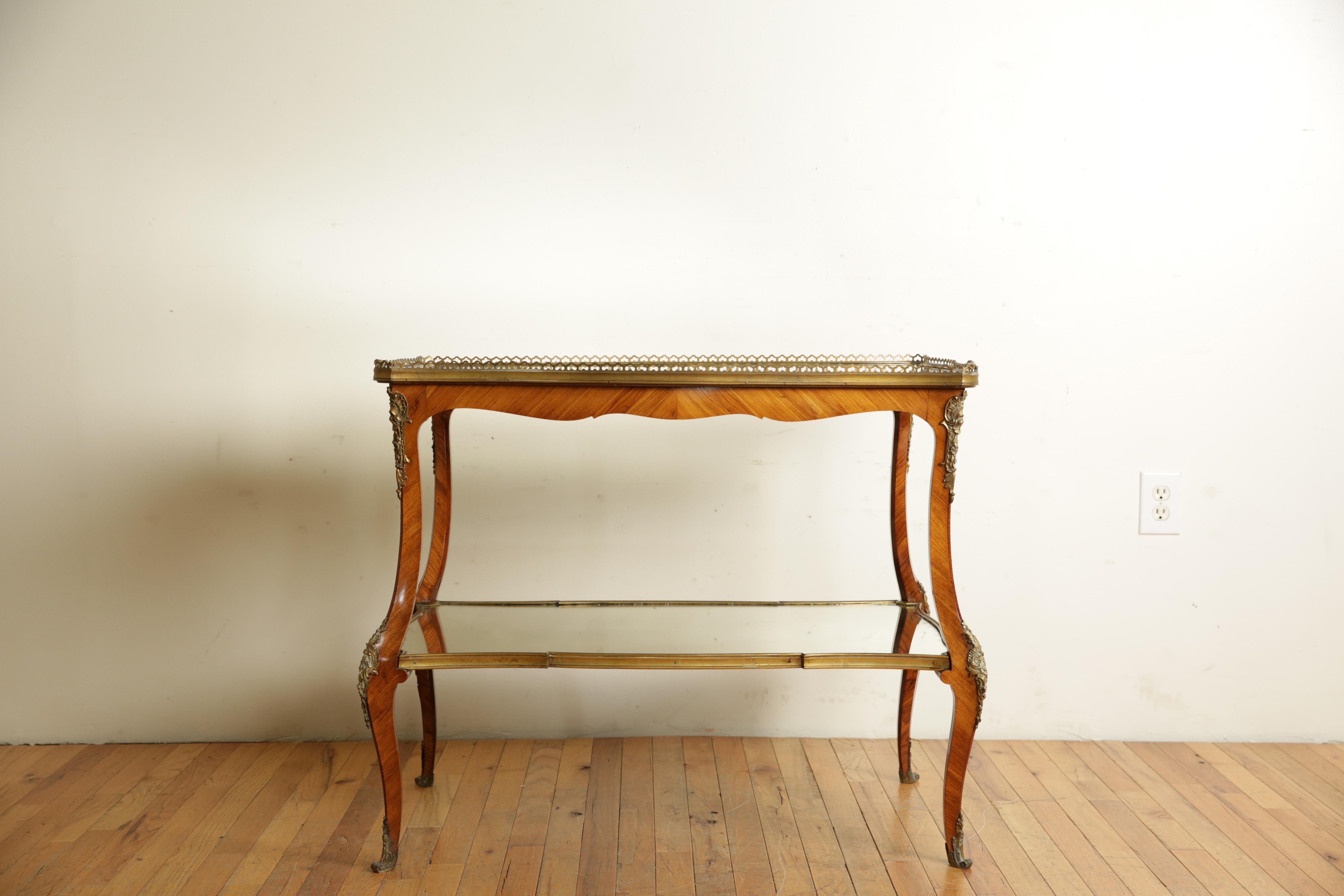 the table having two tiers of serpentine shape, both with mirrored surfaces the upper with a raised brass gallery the lower with a brass border, the cabriole legs mounted with ormolu ornamentations and escutcheons, the handled top is removable
