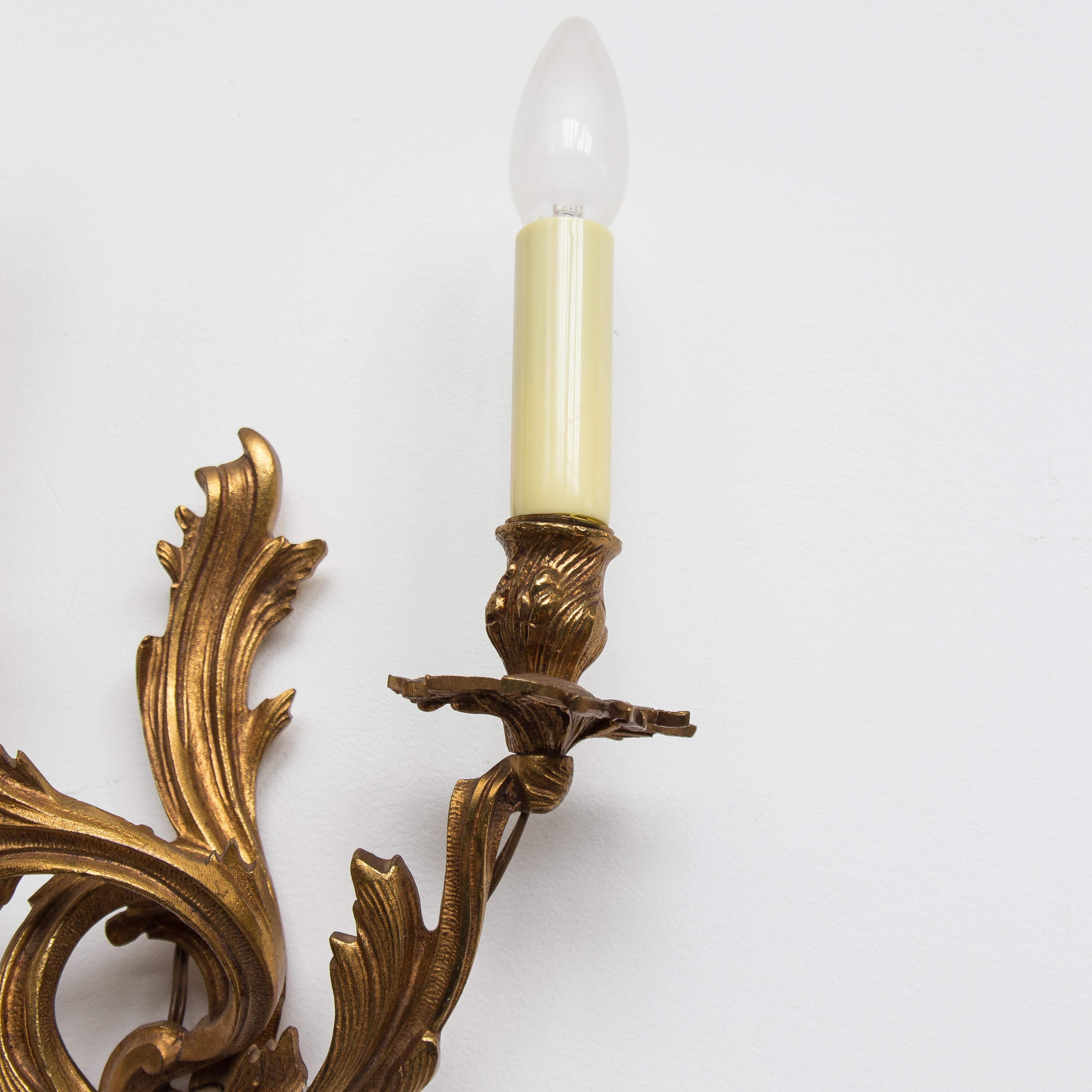 Chiseled and gilt bronze two-light antique wall sconce sculpted with flowing foliage and scrolls in Louis XV style. This Rococo decor is dominated by asymmetrical forms. Lamp fitting E14.