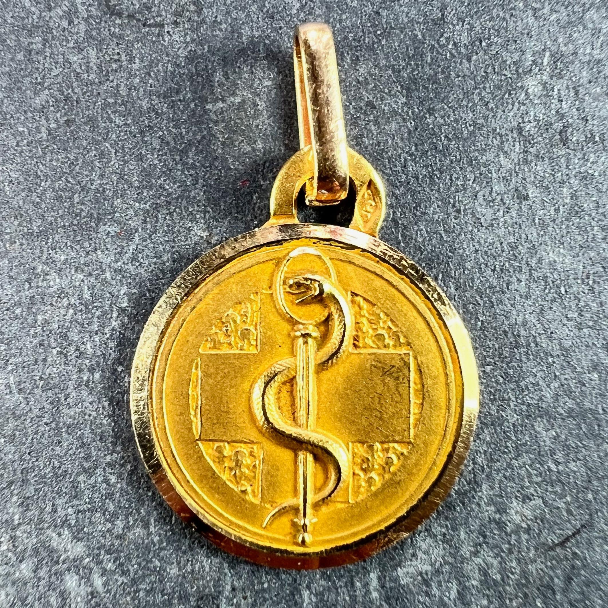 An 18 karat (18K) yellow gold charm pendant depicting a snake entwined around a staff representing the medical Rod of Asclepius on a cross to one side, the other side with the words 'Groupe Sanguin Rhesus' for engraving with the wearer's blood type.
