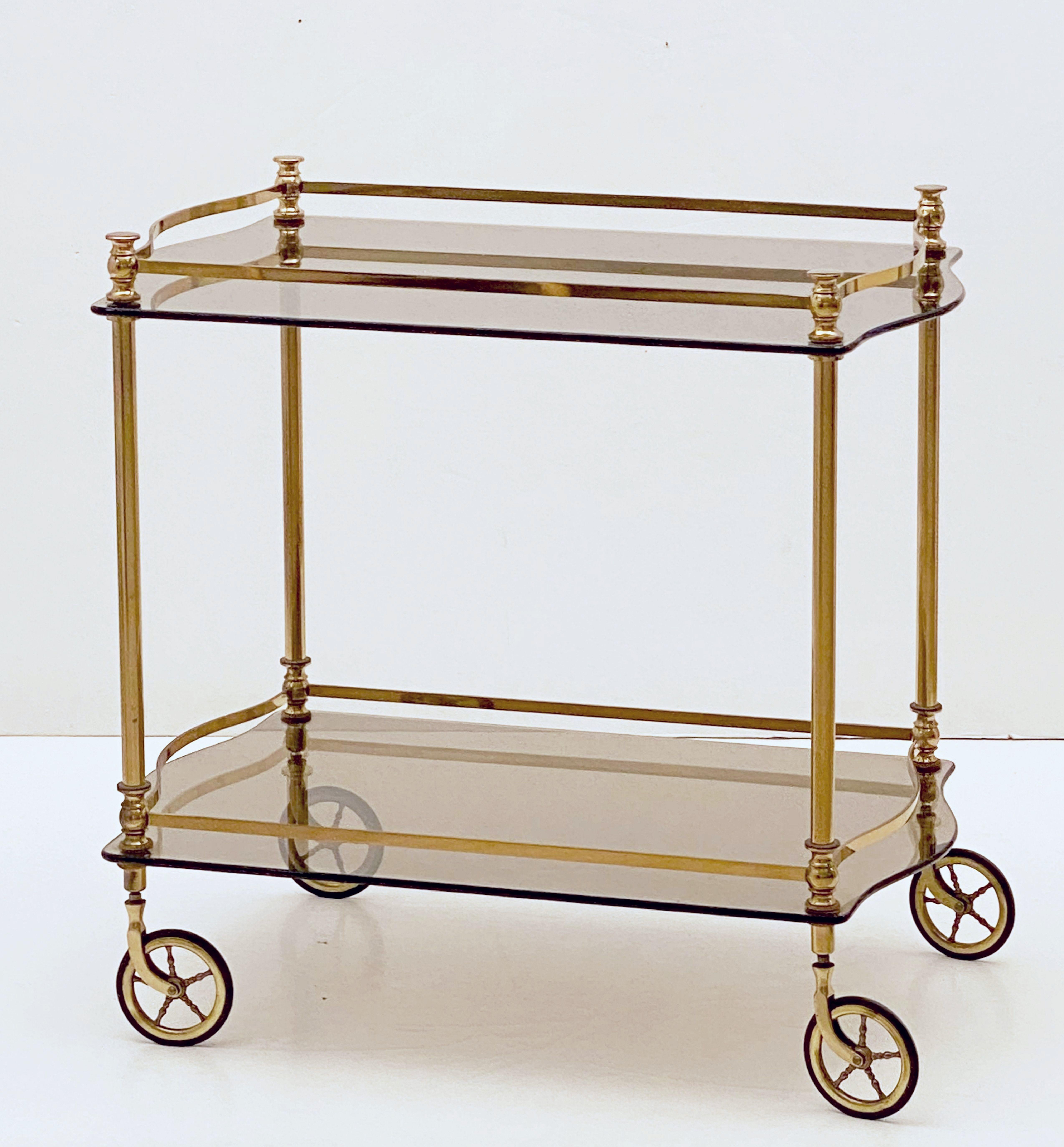 A handsome vintage French rectangular bar cart table or serving trolley for drinks in brass, featuring two tinted glass tiers, each tier with stylish serpentine gallery, resting on rolling spoked caster wheels. 

Perfect for use as a side or end