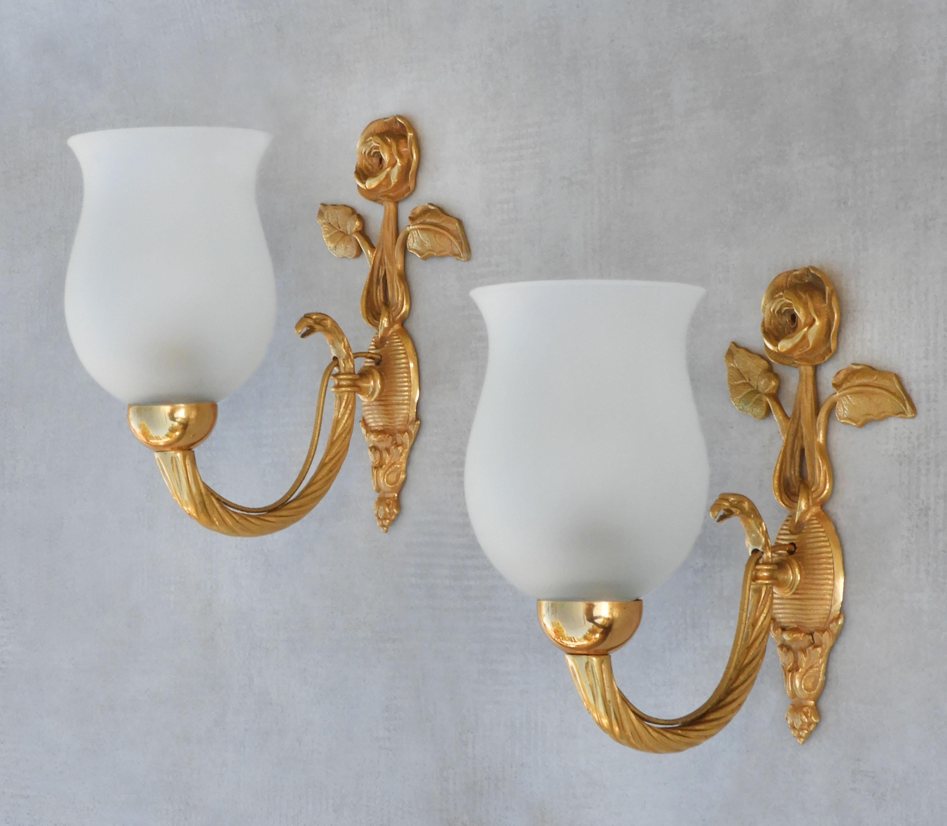 A beautiful pair of sconces from France C1950. Charming French wall lights in gilded brass and frosted glass. Mid-century empire revival featuring a rose bloom and eagle's head, a stylish modern take on a timeless classic design. Well-made,