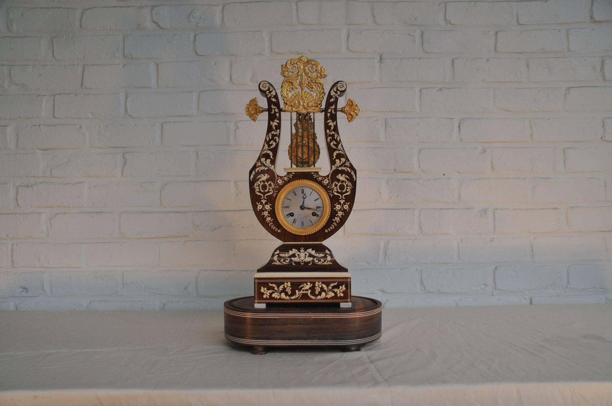 Restoration period, circa 1830, stamped Thevenard.
On original stand, under domed glass.

French Charles X period ormolu-mounted rosewood bone inlaid portico mantel clock. Inlaid overall with floral sprays and birds. Rare lyre shaped. The silvered