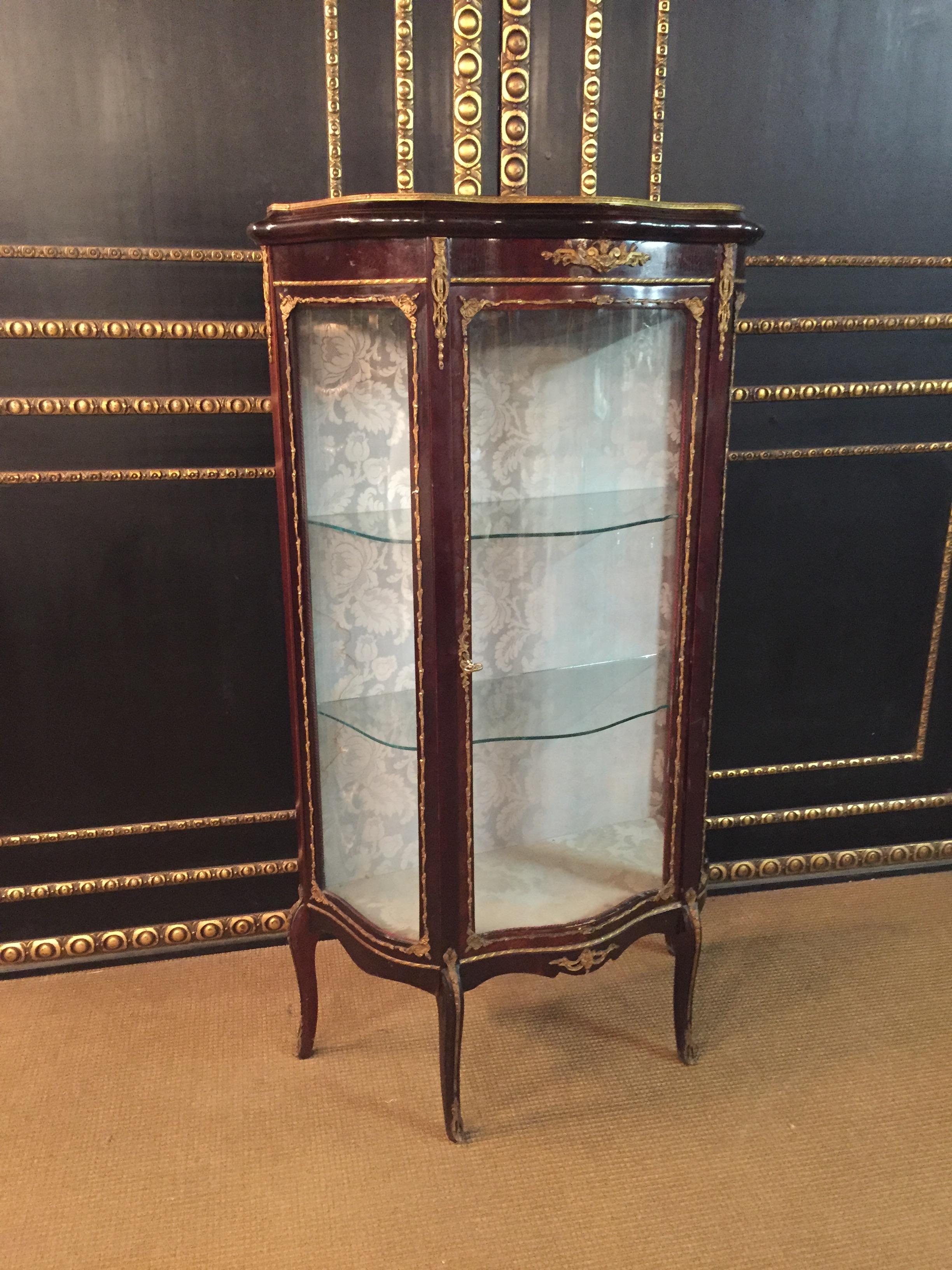 Delicate French vitrine rosewood on solid wood. High-rise, one-door, cambered and three-sided glazed body. On curly feet scalloped out. Three-sided glazed vitrine. Slightly protruding top plate with brass gallery. Rich bronze fittings. Backboard