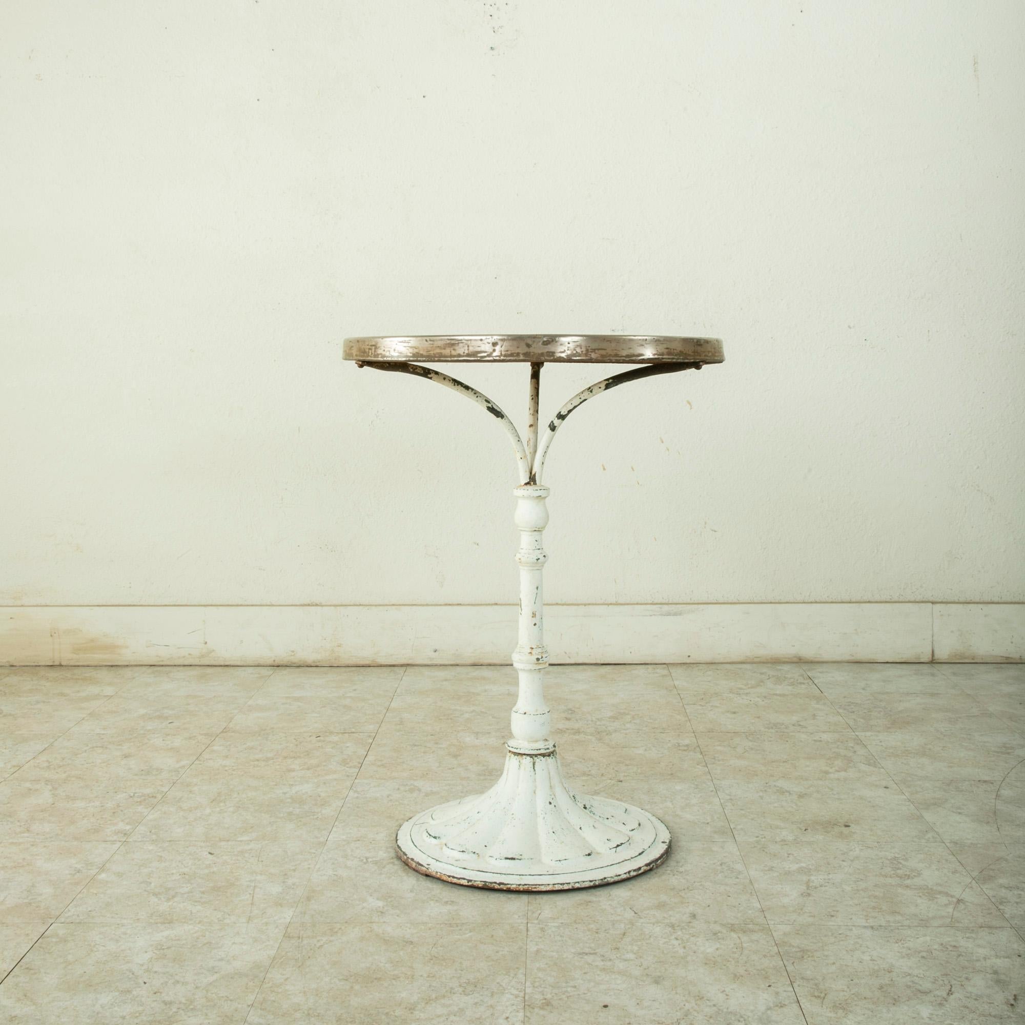 This French round bistro table from the turn of the twentieth century features an iron pedestal base and a white marble top. The marble is trimmed in brass and joins the base with three arm supports. The base is painted white with a patina that