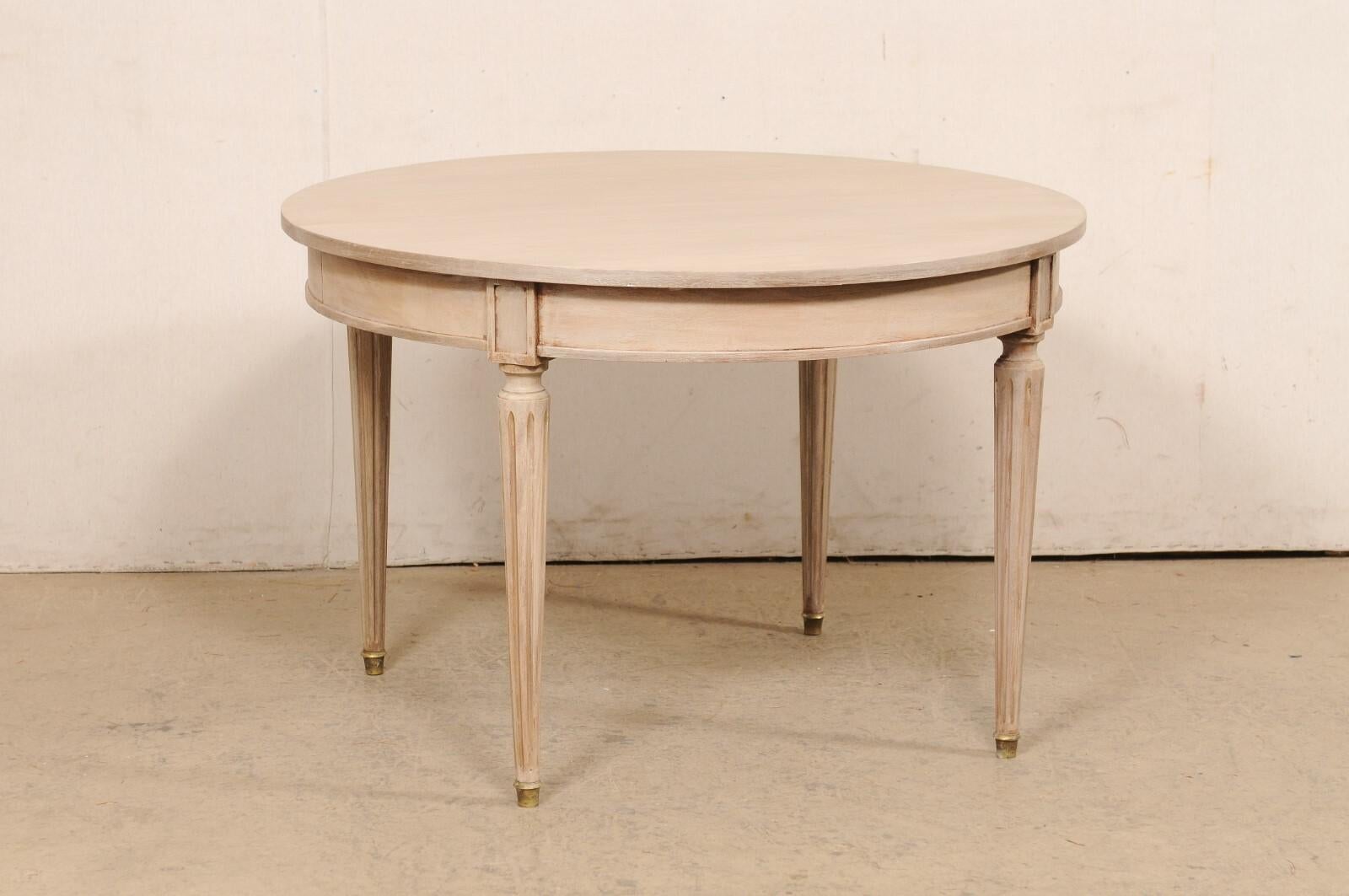 A French painted wood center table from the mid 20th century. This vintage table from France features a circular-shaped top, which slightly overhangs the rounded apron below with cleanly molded skirt and framed rectangular plaques at each knee. The
