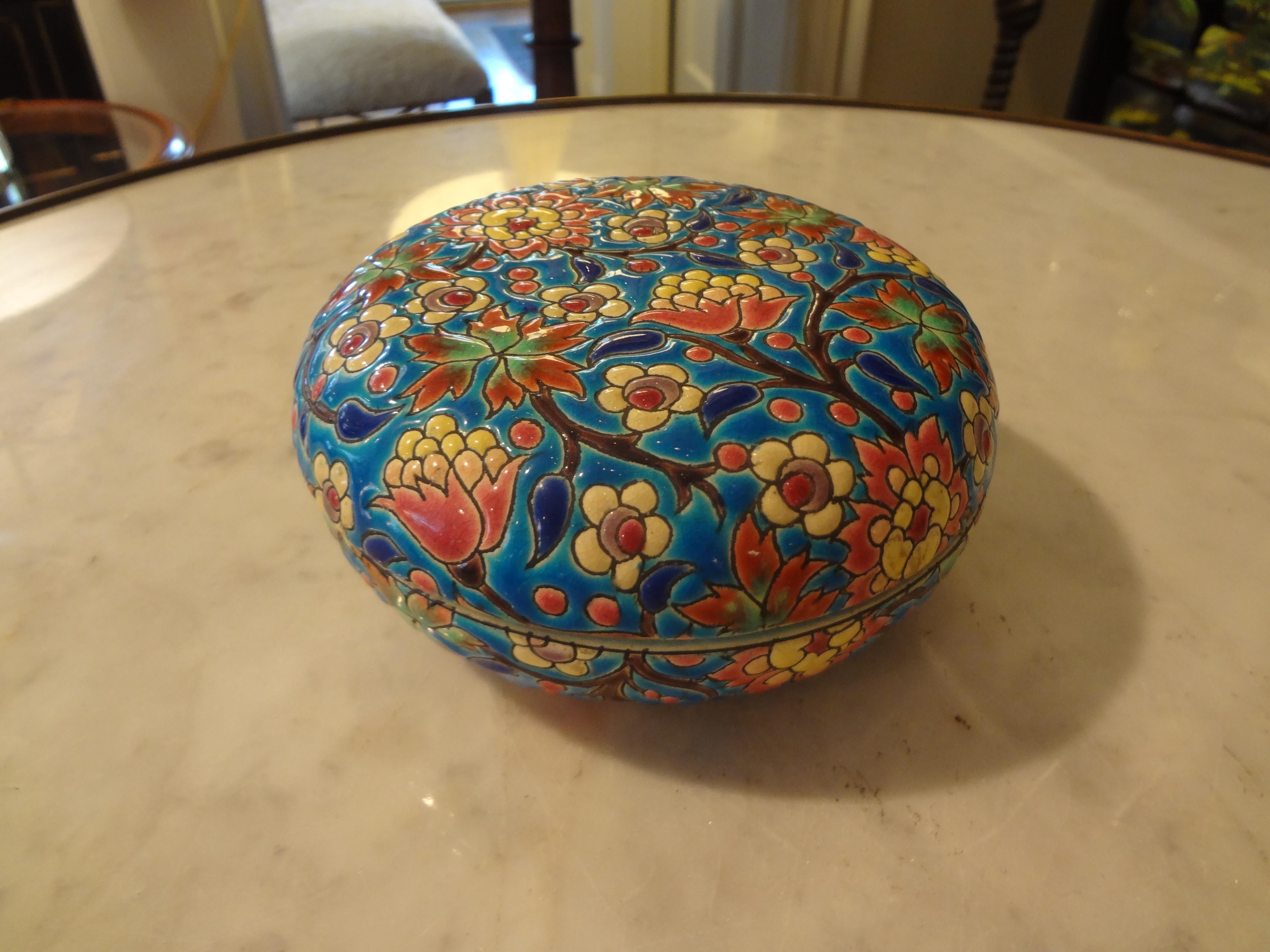 French faience round decorative box or trinket box from the Emaux de Longwy art pottery workshop in France. This porcelain box is hand-decorated with a colorful enameled glaze in a cloisonné style chinoiserie design. The decoration consists of