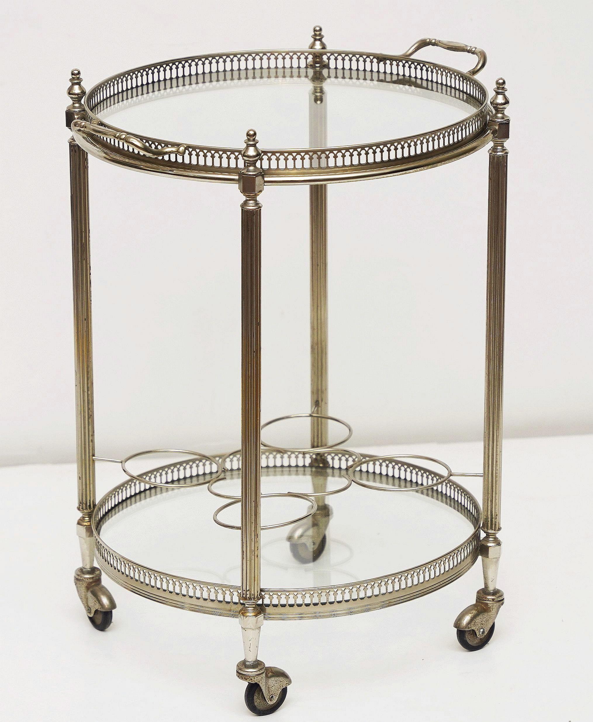 Bonito carrito de bebidas o carrito de bar francés, de níquel y cristal, de la época moderna de mediados de siglo, con dos pisos redondos, cada uno con galería calada y cristal, montados en un armazón con cuatro ruedas pivotantes.

La galería