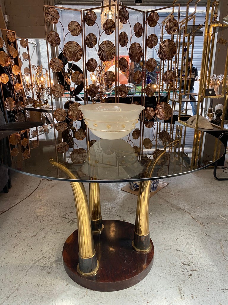 Very beautiful French round table glass smoked brass, the base mahogany veneered is made of three brass bases imitating elephant tusks. 
Glass diameter 1m20, table height 80 and base diameter 59 cm. This table can be used as a dinner table or look