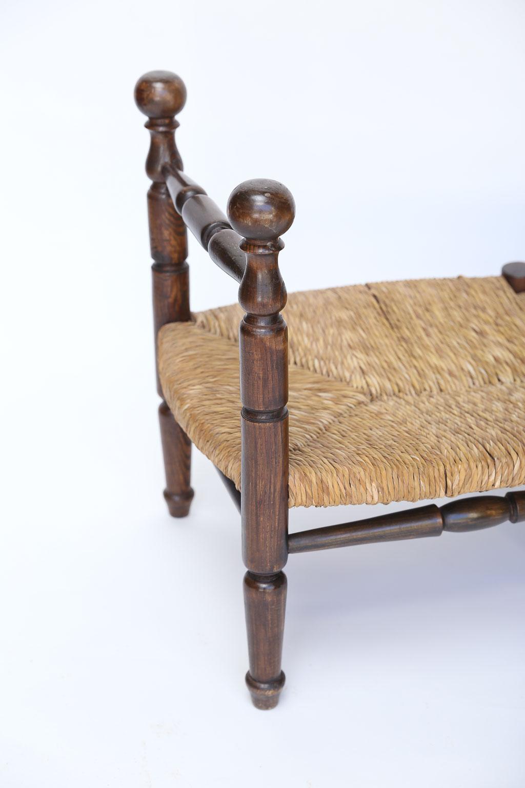 An antique rush seat bench found in France. With turned arms, turned legs and rush that has aged to a beautiful color, the overall look of this piece is beautiful.