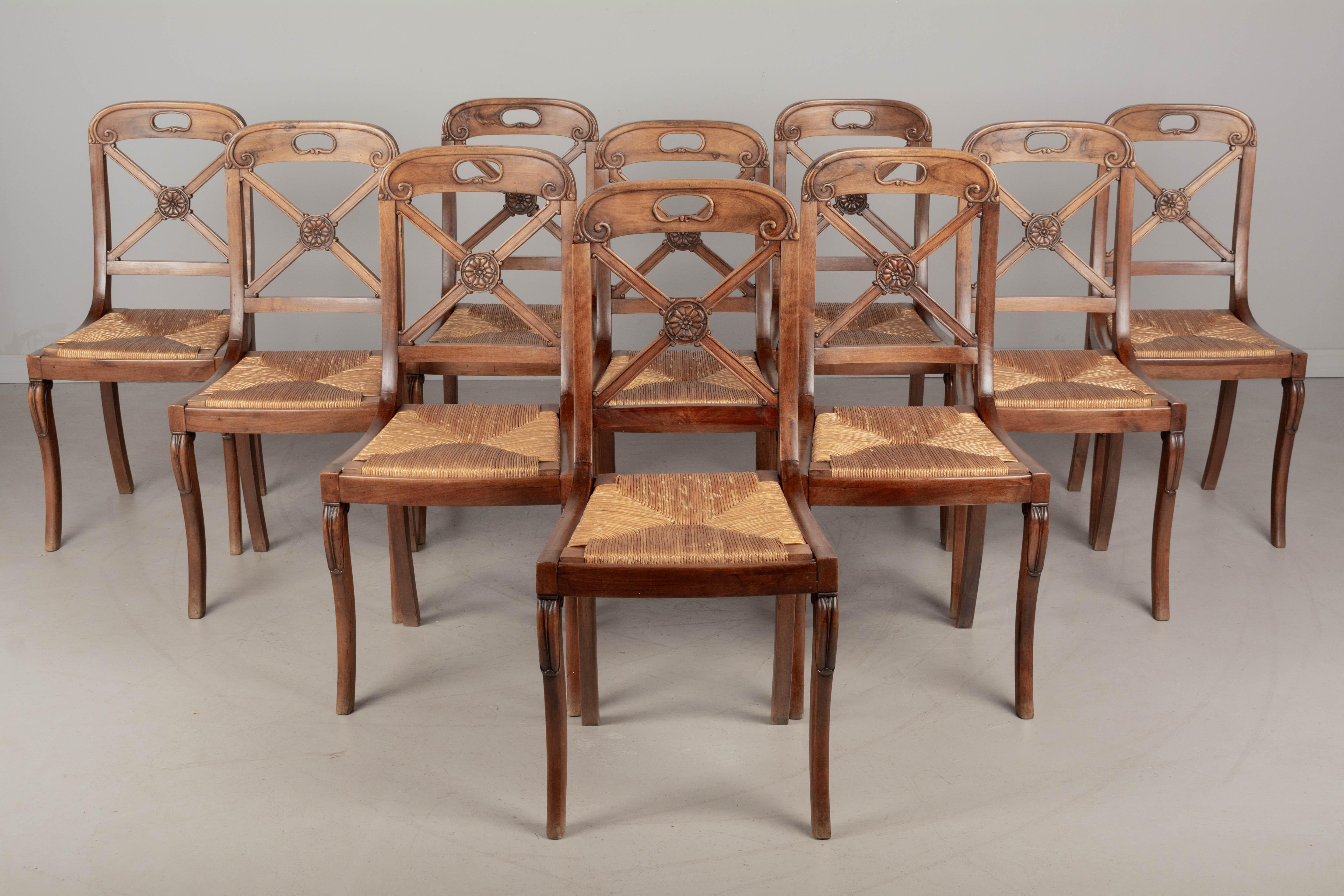 A set of ten French Restauration style dining chairs with walnut frame and natural rush seat. Carved rosette detail and handle at the top. Chairs are sturdy and the removable rush seats are in good condition. Circa 1950s
Overall dimensions: 17.25