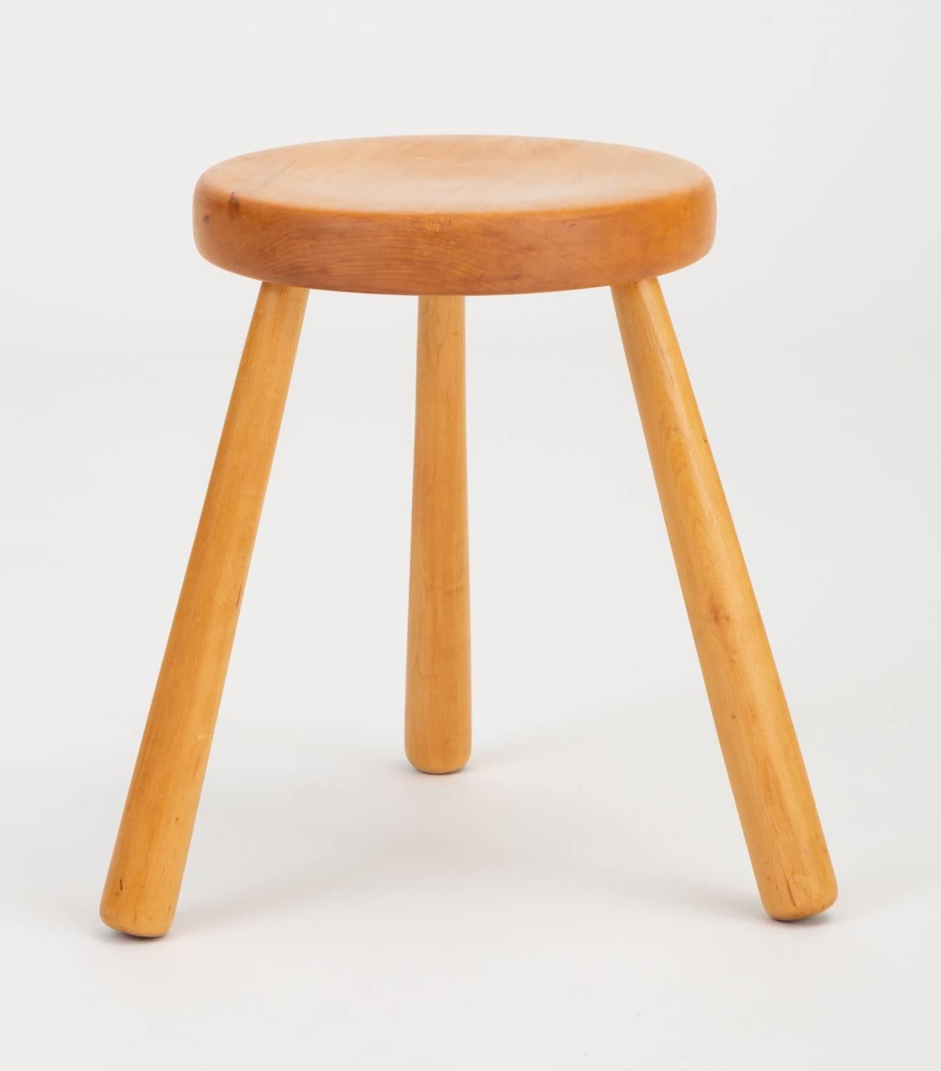A small, three-legged stool in turned pinewood similar to the rustic modern designs by Charlotte Perriand for the Les Arcs ski chalet in 1968. This example has a tripod base for optimal stability, and a slightly bowed seat for comfort. The turned
