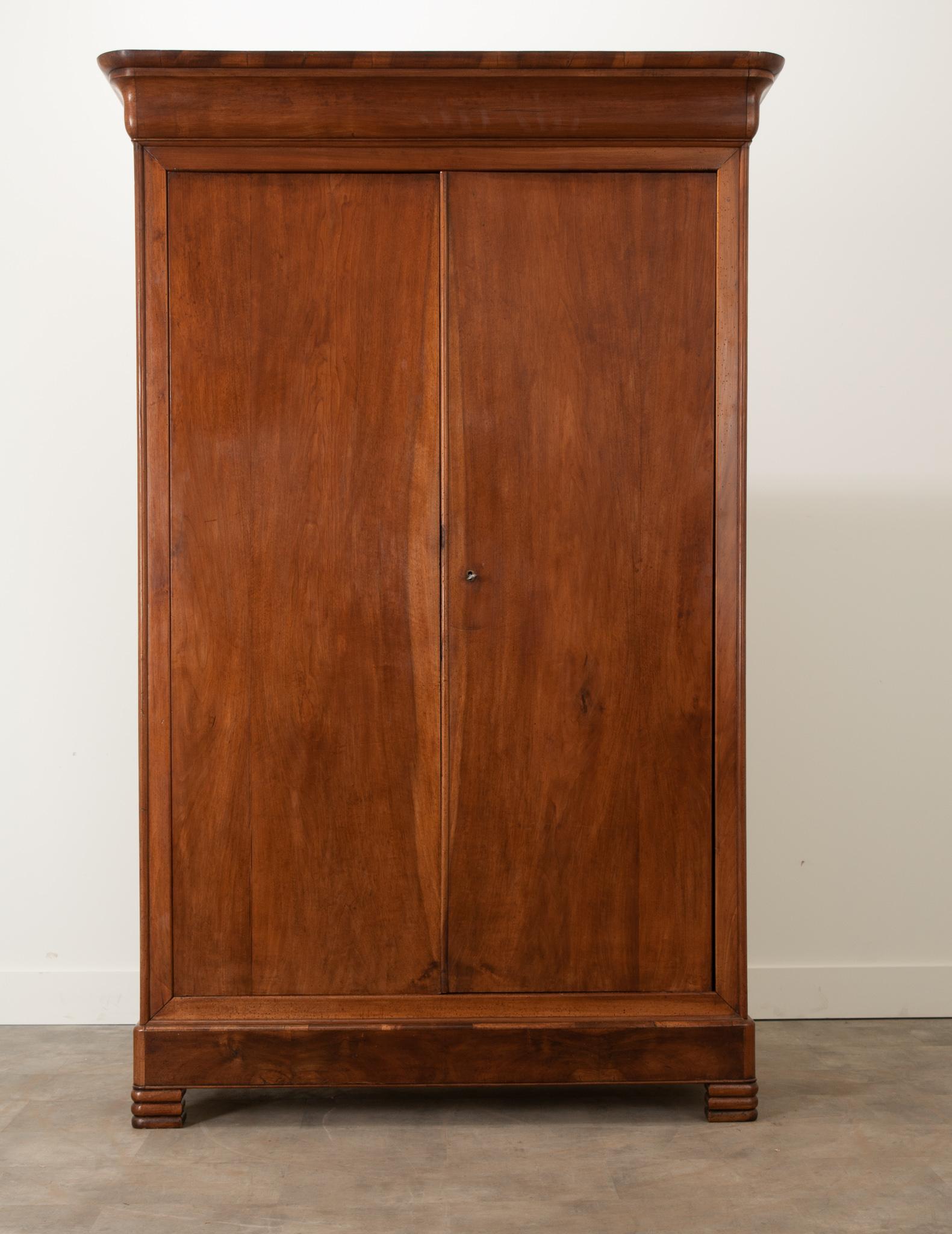 A handsome 19th century walnut armoire, made in France in the Louis Philippe style. This tall case antique has a simple, linear composition – an attribute that makes Louis Philippe pieces ideal for their versatility and placement possibilities. This