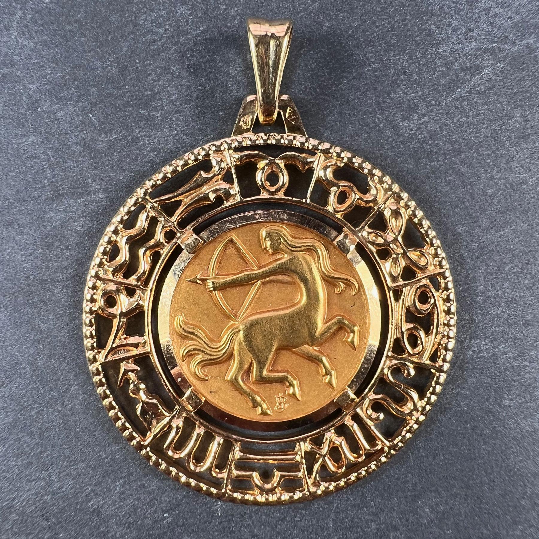 An 18 karat (18K) yellow gold charm pendant designed as a pierced medal of the Zodiac starsign for Sagittarius, signed JB, surrounded by a frame depicting the symbols of the other Zodiac starsigns. Stamped with the eagle mark for 18 karat gold and