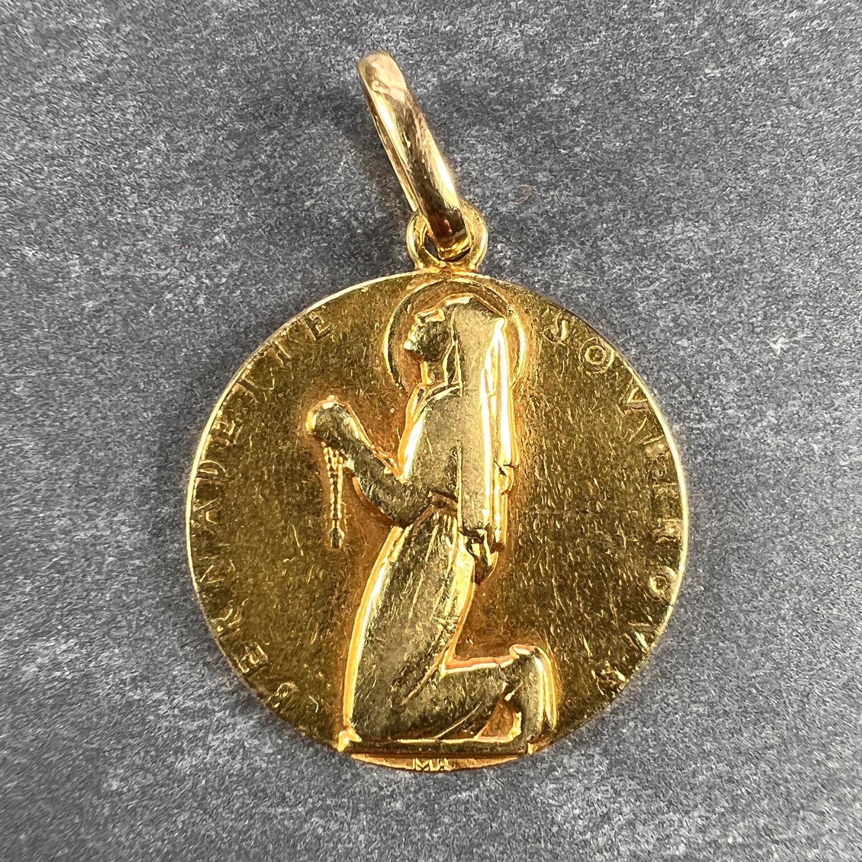 A French 18 karat (18K) yellow gold charm pendant  designed as a medal depicting Saint Bernadette (the patron saint of Lourdes) at prayer with the words Bernadette Souberous around the edge. Stamped with the eagle mark for 18 karat gold and French